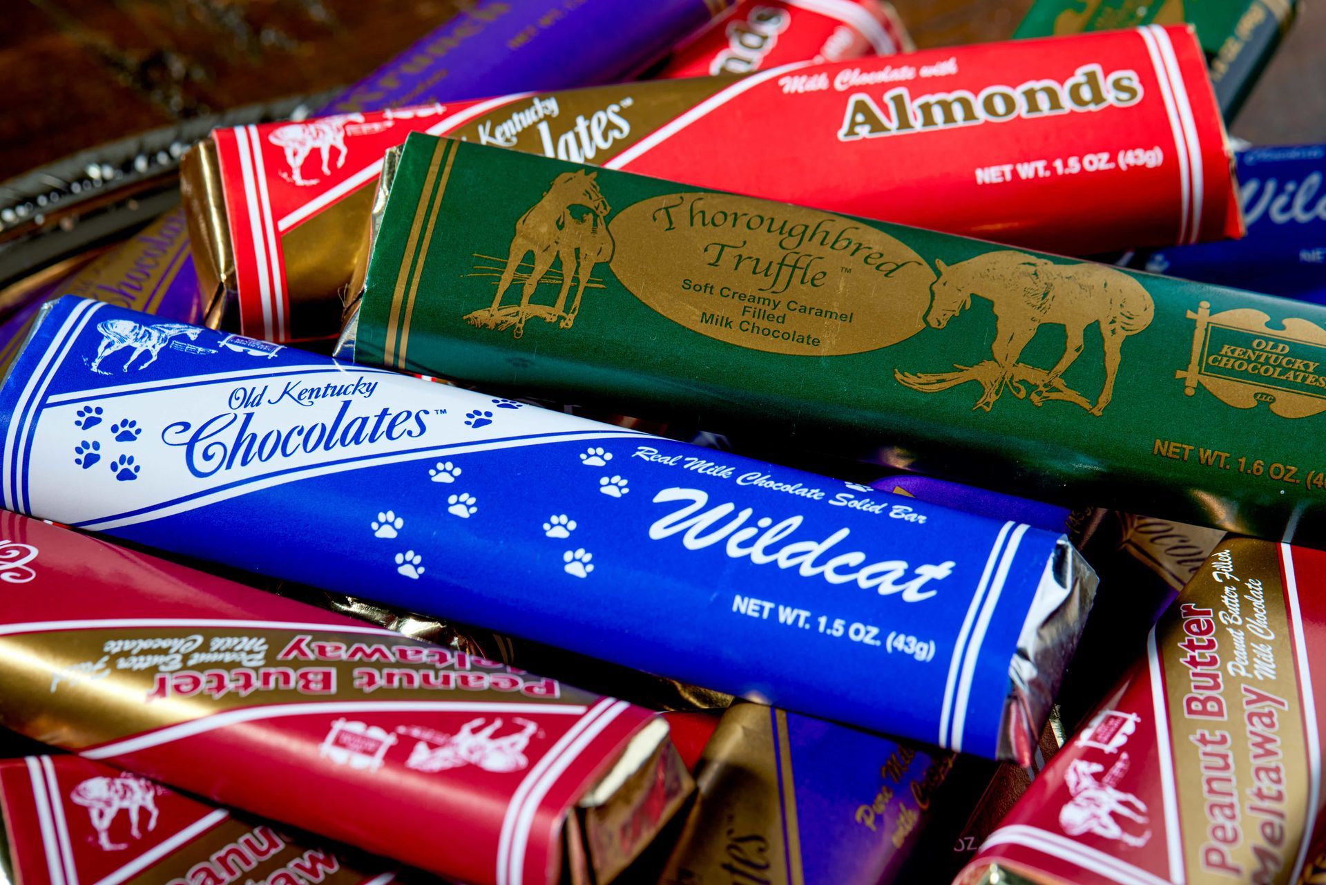 A colorful pile of various Kentucky Chocolates bars with logos and flavor labels including Wildcat and Almonds.