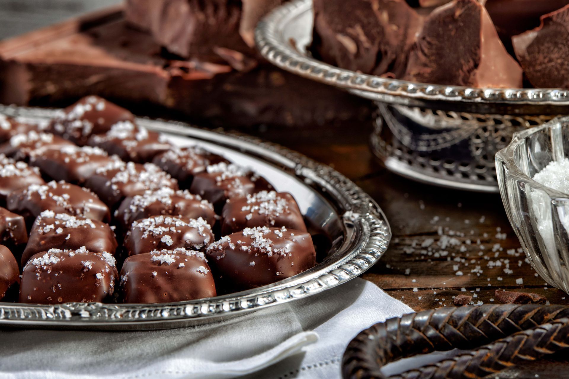 Chocolate-covered caramel candies with sea salt on a silver platter. One candy is cut, revealing the caramel center.
