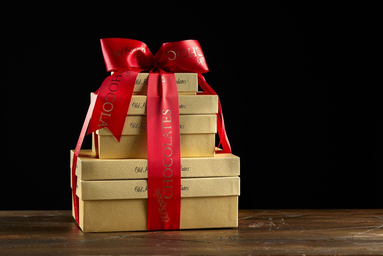 Gold gift boxes stacked and tied with a red ribbon and bow on a wooden surface against a black background.