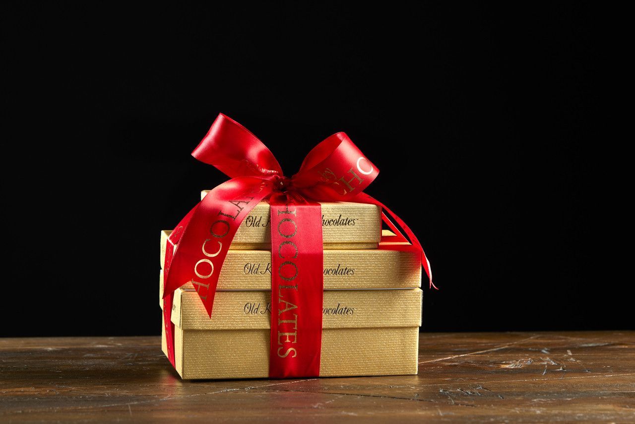 Stacked gold gift boxes with a red ribbon and bow.
