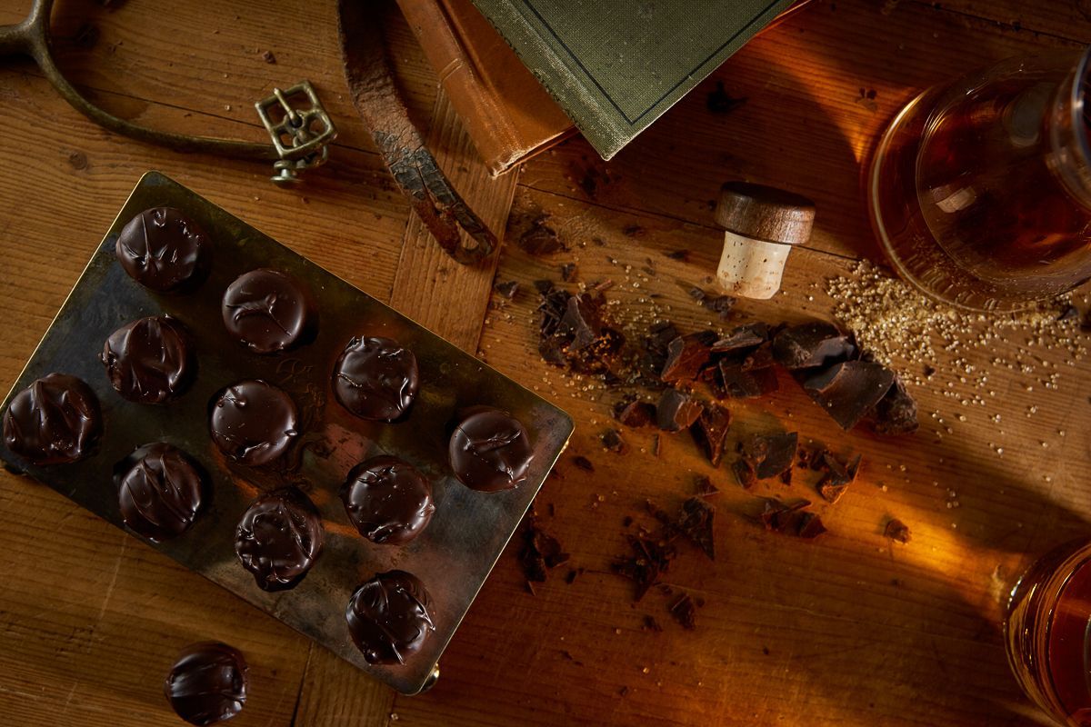 A dark, rustic tabletop featuring a partially used blister pack of black pills, a bottle stopper, and spilled herbs.