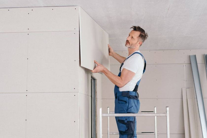 Worker installing drywall in a room with a ladder nearby