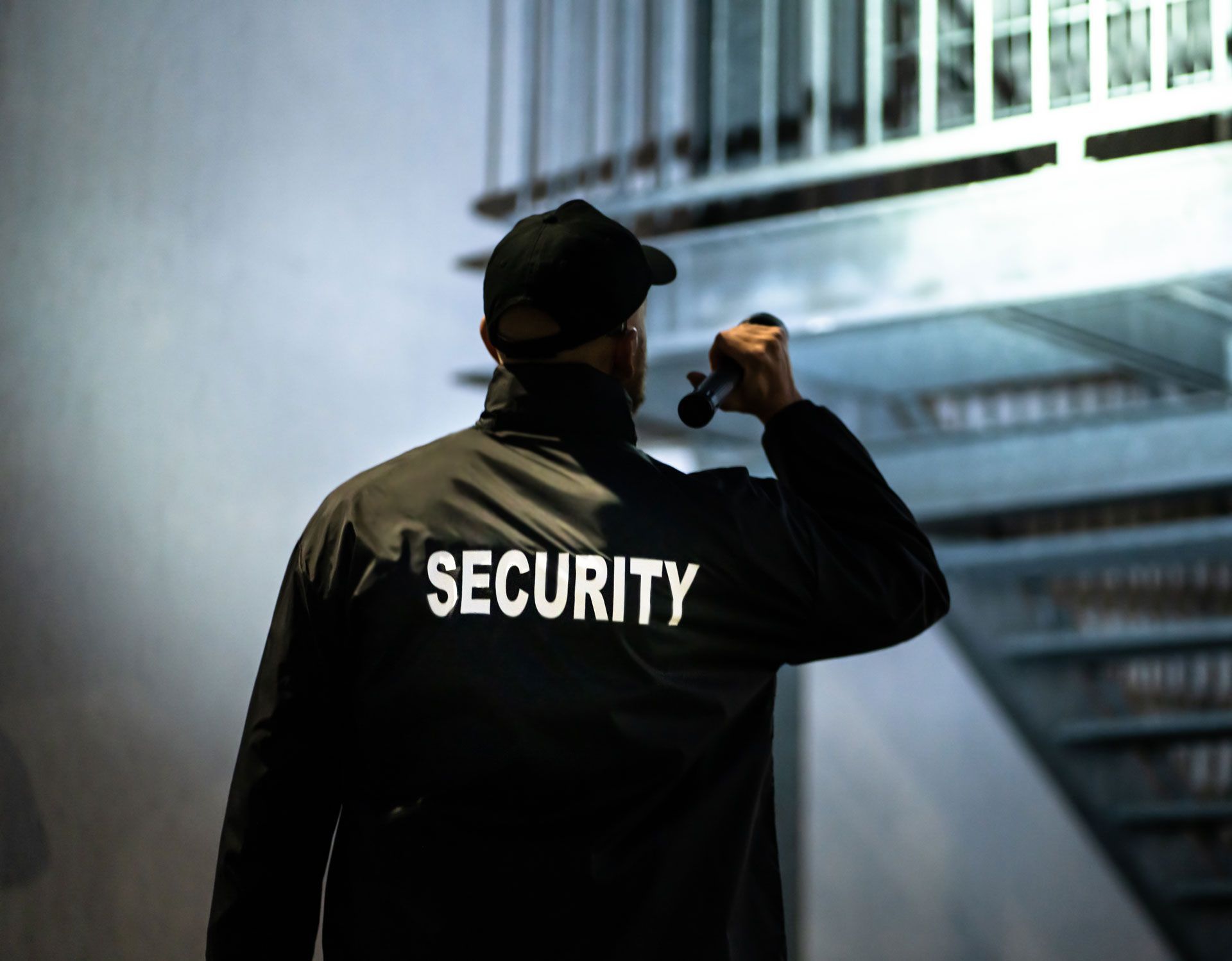 Security guard walking in a dim stairwell, holding a flashlight with “SECURITY” on his jacket.