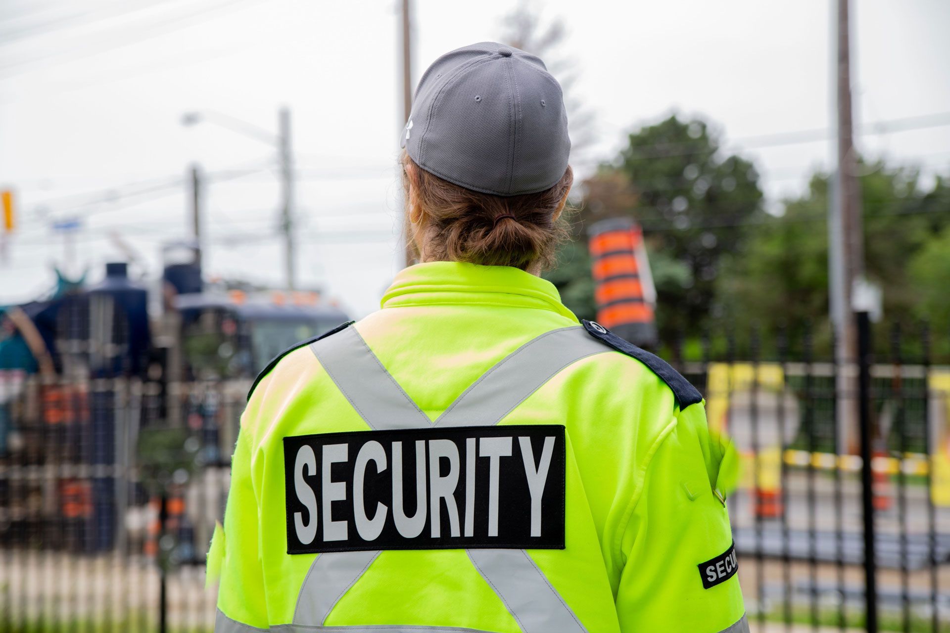 Security guard in neon yellow jacket with reflective stripes, seen from behind at a worksite.