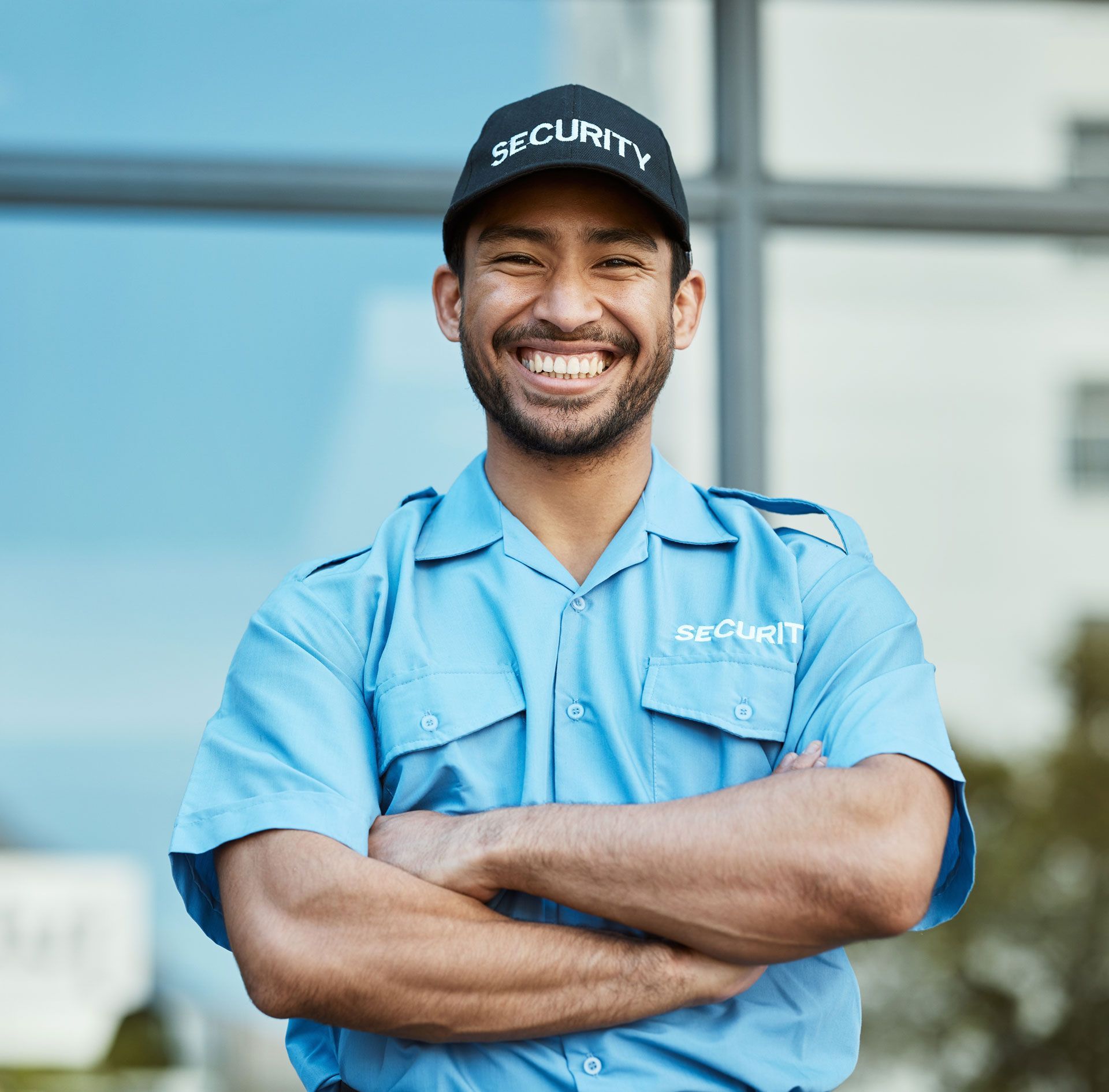 Smiling security guard in blue uniform and cap, arms crossed outdoors