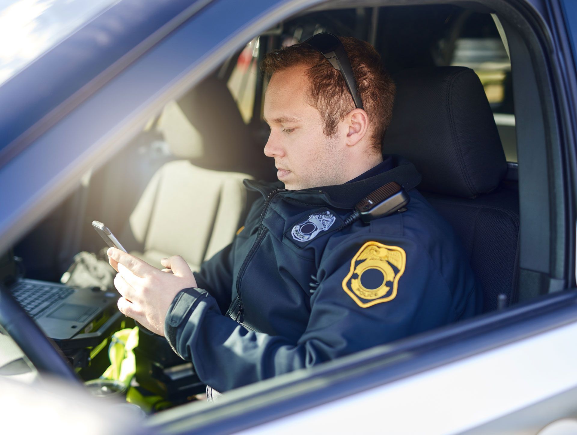 Police officer using a phone while sitting in a patrol car