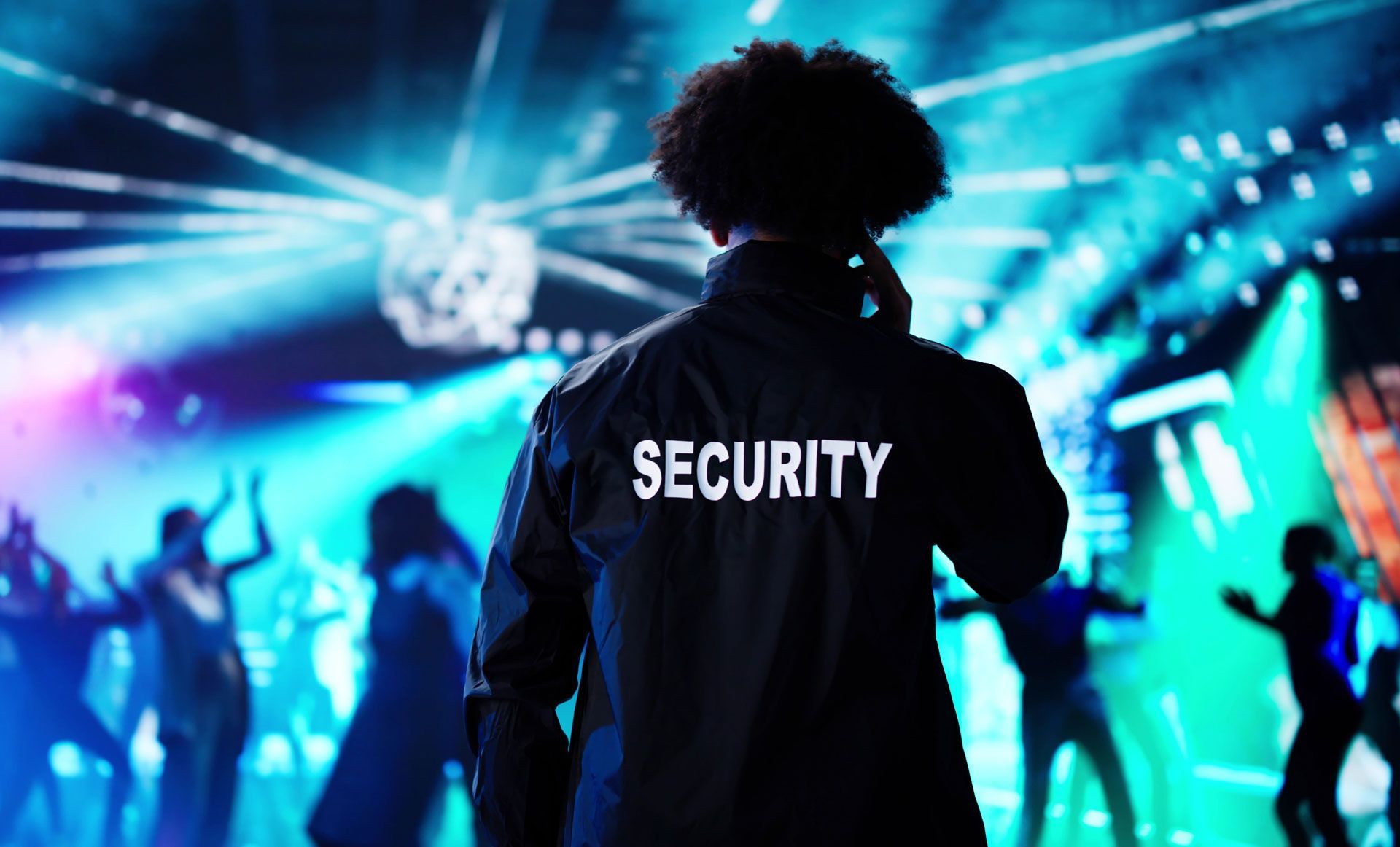 Security guard facing a blue-lit concert crowd with stage lights in the background