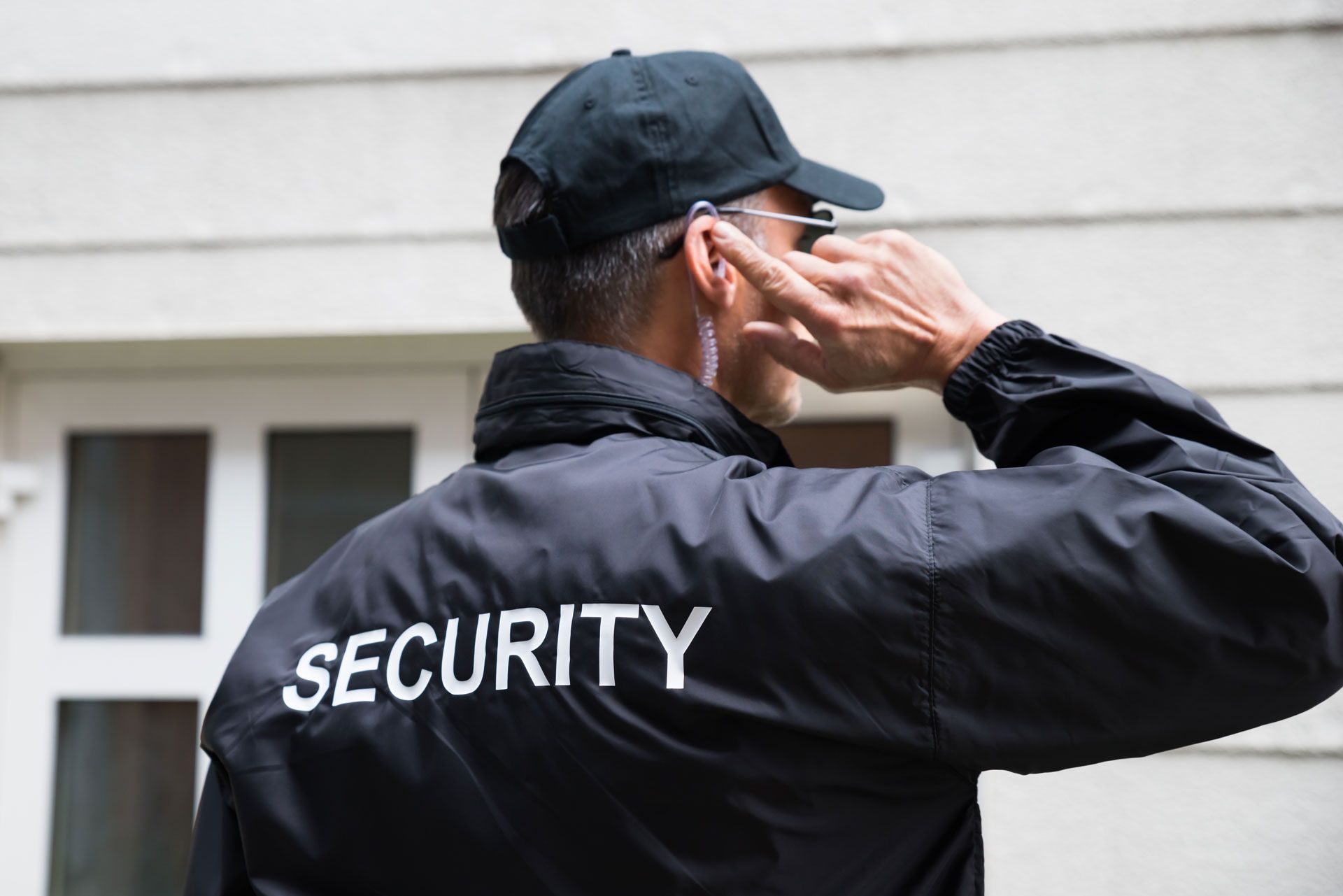 Security guard in black jacket and cap saluting outside a building