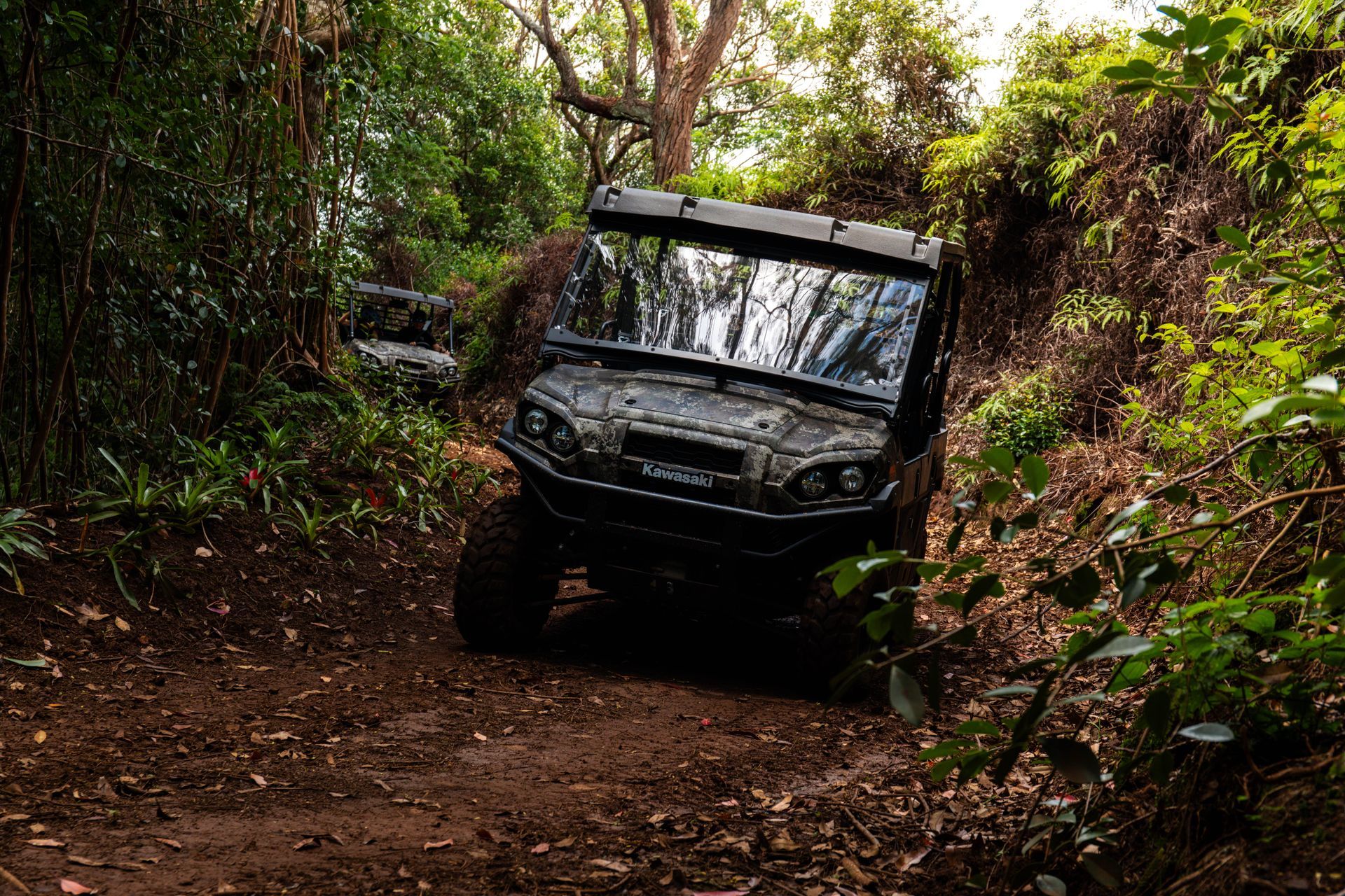 Off-road utility vehicle driving through a muddy forest trail surrounded by dense greenery