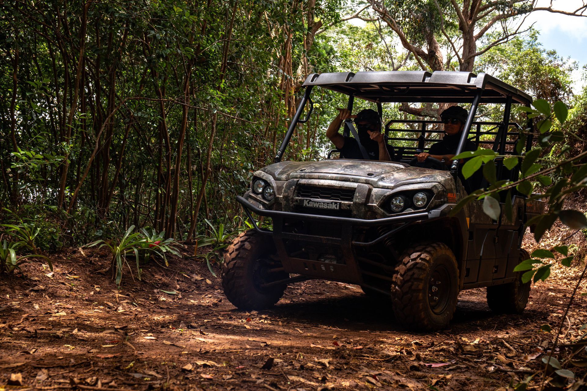 Off-road utility vehicle driving through a muddy forest trail, surrounded by dense green trees.