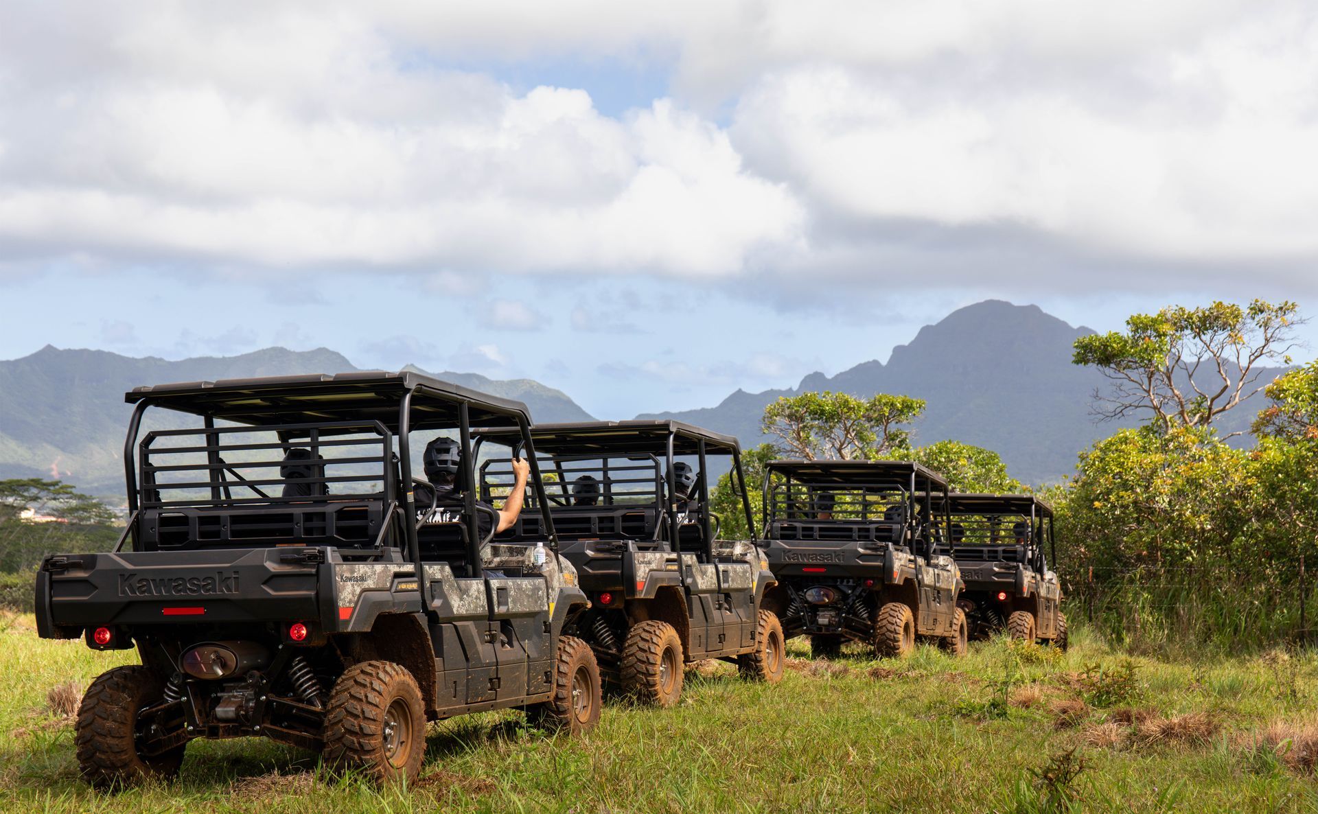 Safari jeeps lined up on a grassy plain with mountains and clouds in the background