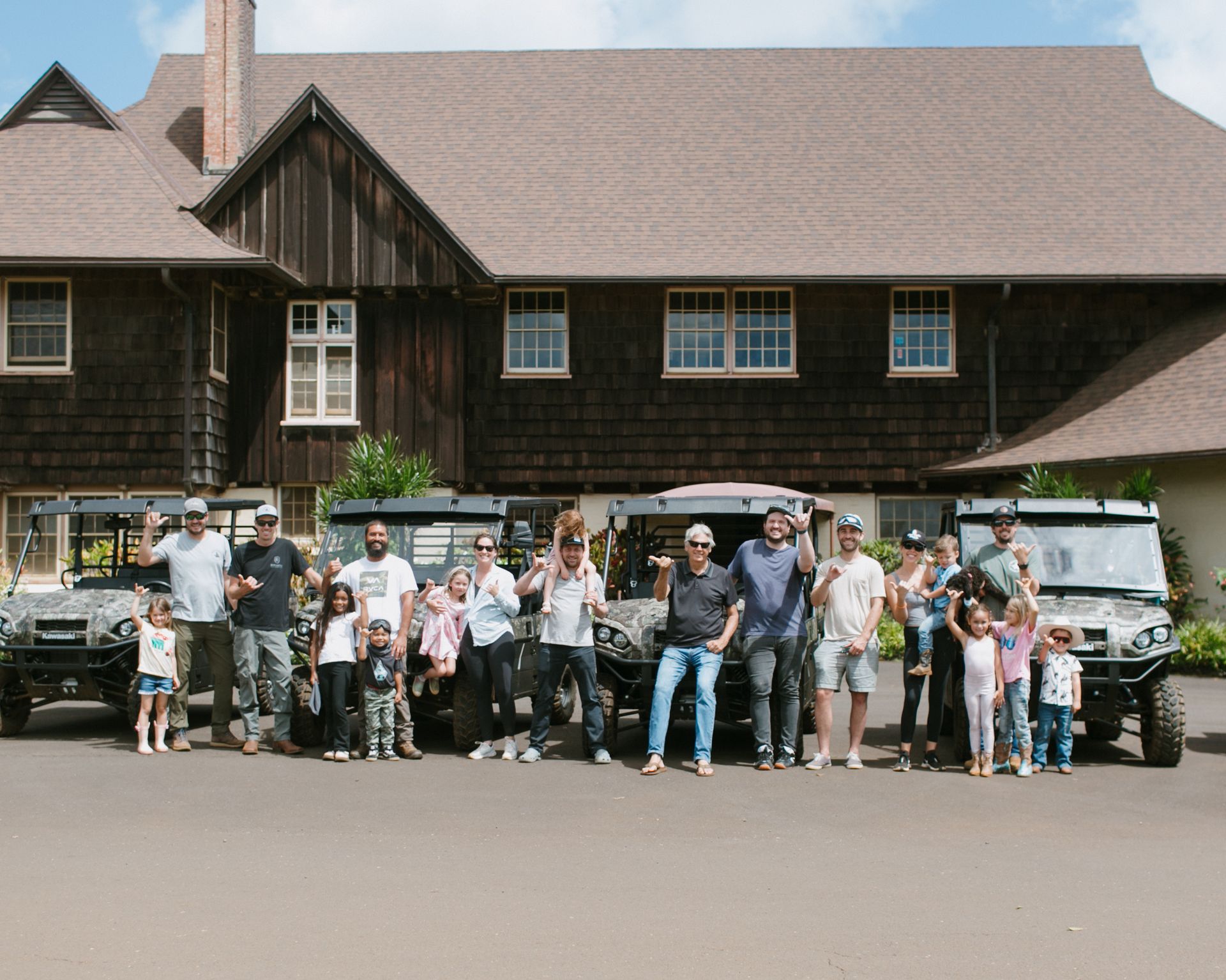 Group posing in front of a rustic lodge with two parked SUVs under a covered porch