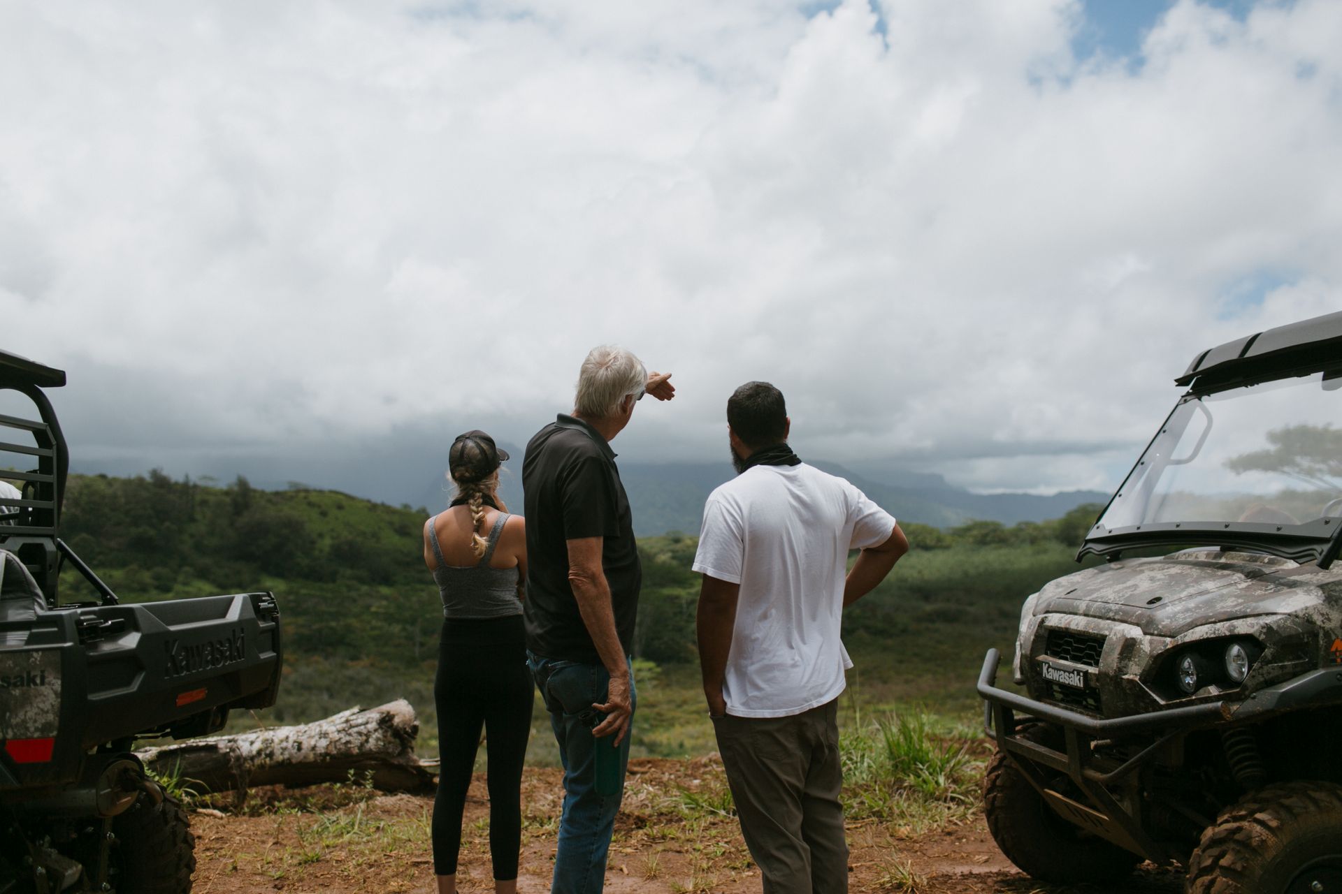 Three people stand by off-road vehicles overlooking a cloudy mountain valley.