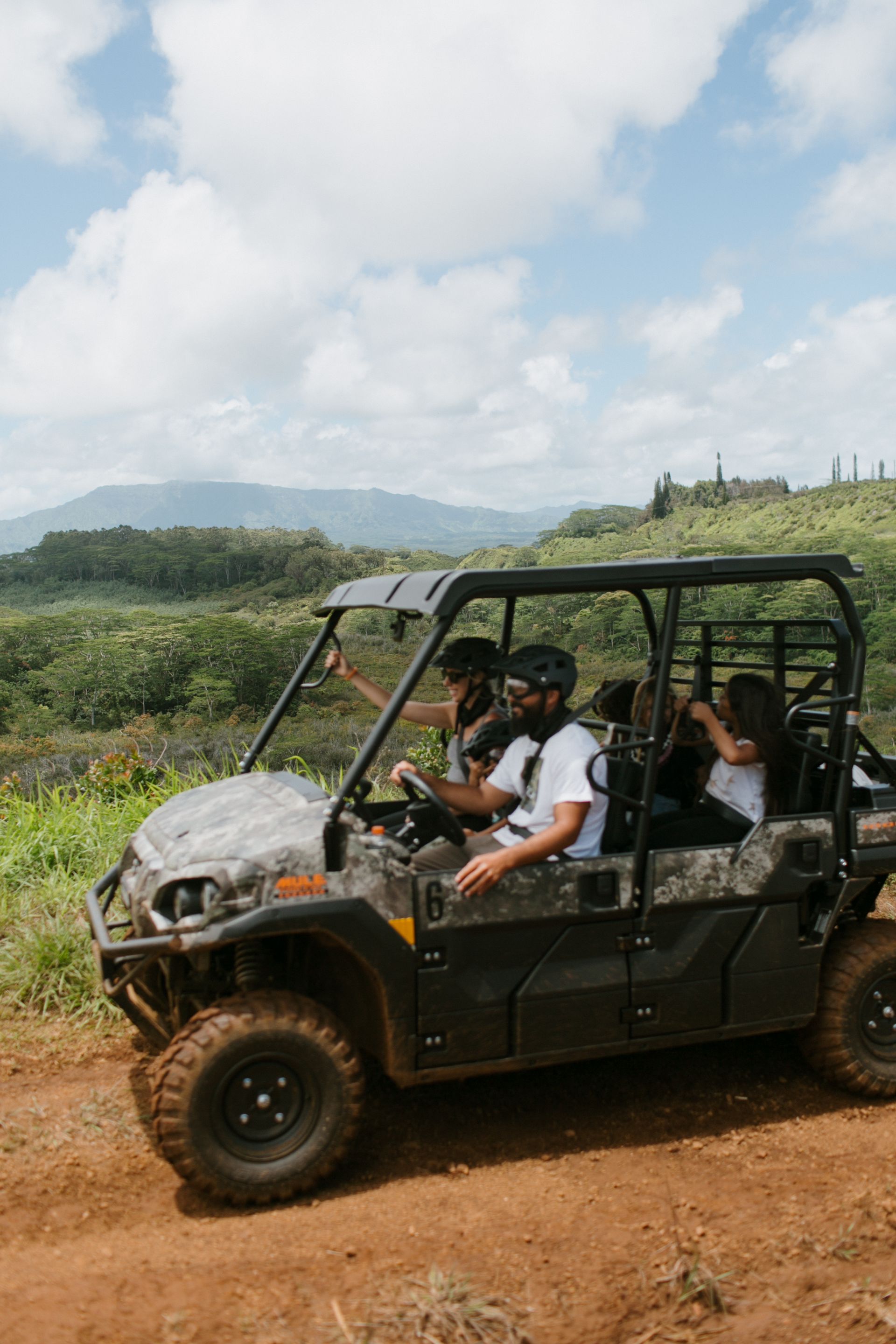Off-road buggy with passengers driving on a dirt trail in a grassy rural landscape