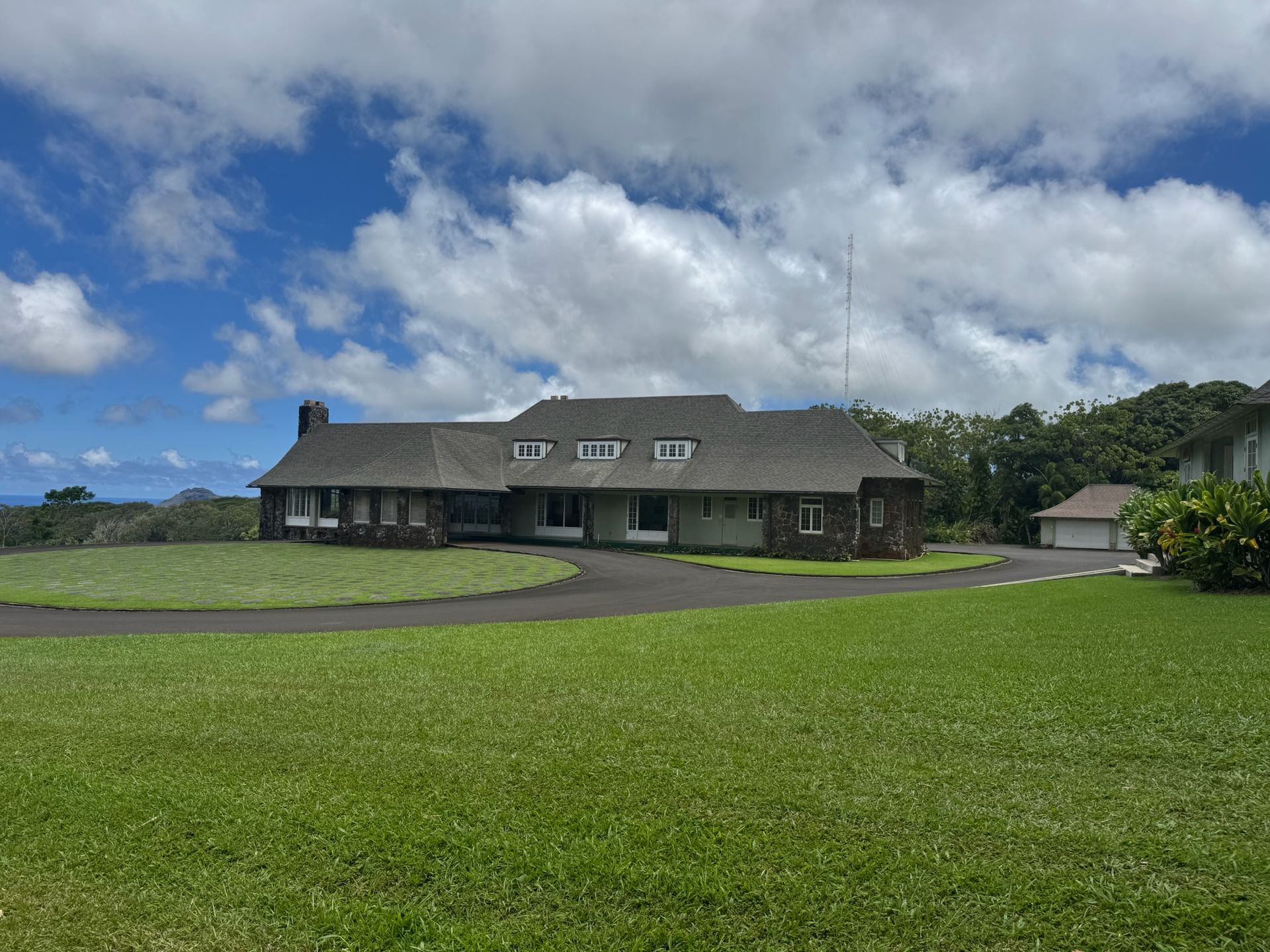 Large green lawn with a dark-roofed house under a cloudy blue sky