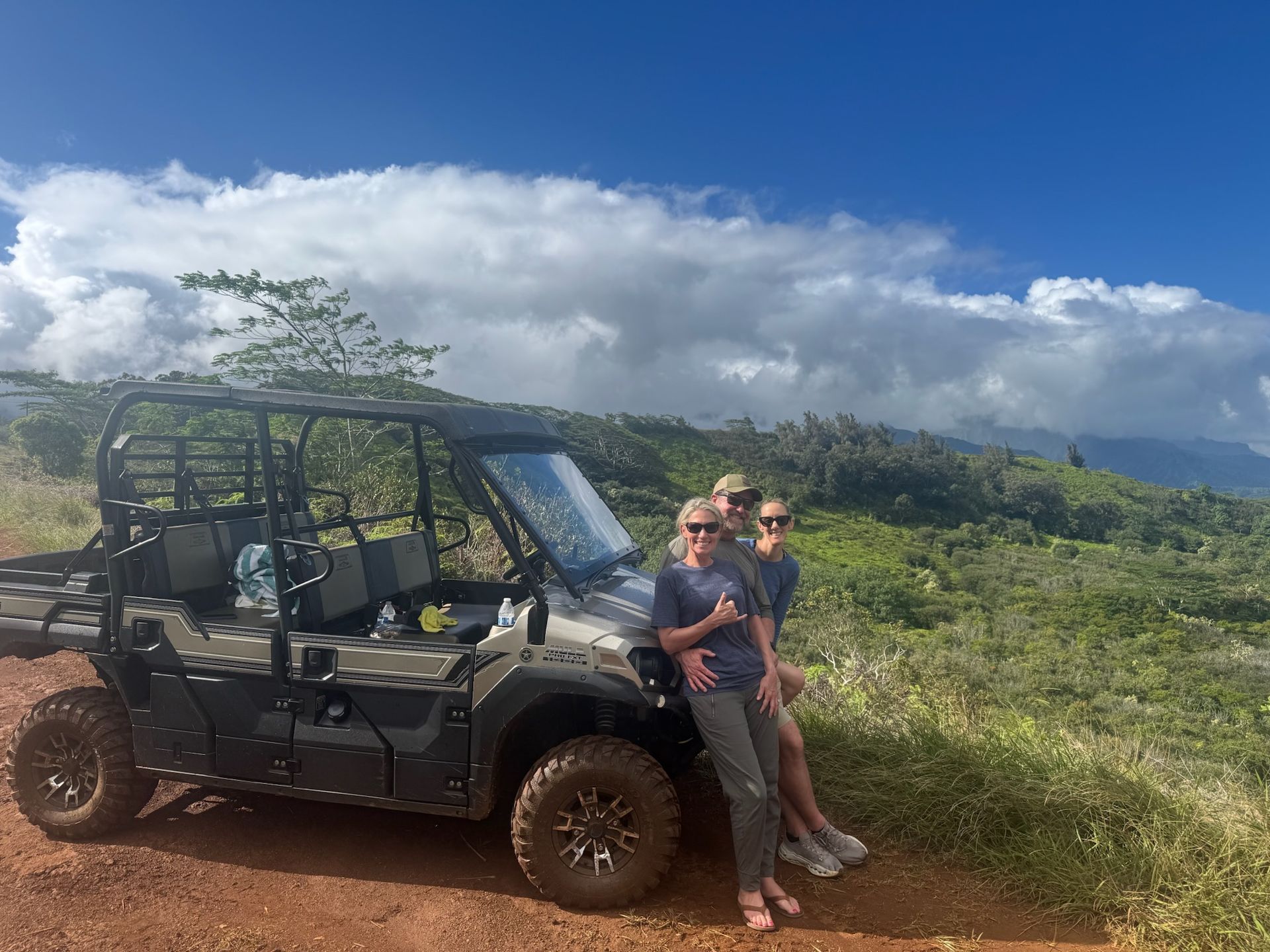 Two people standing by a black off-road vehicle in a grassy field under a cloudy sky