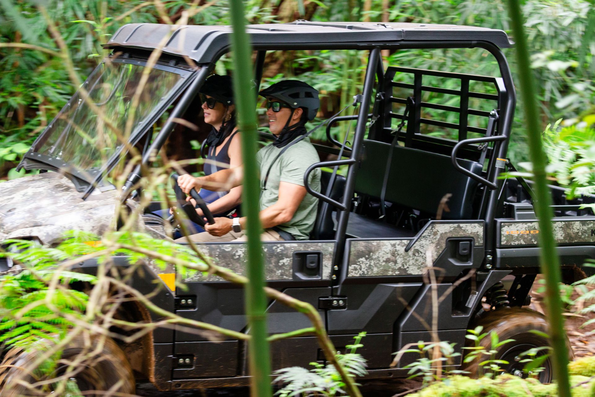 Off-road utility vehicle with two people driving through dense green forest foliage