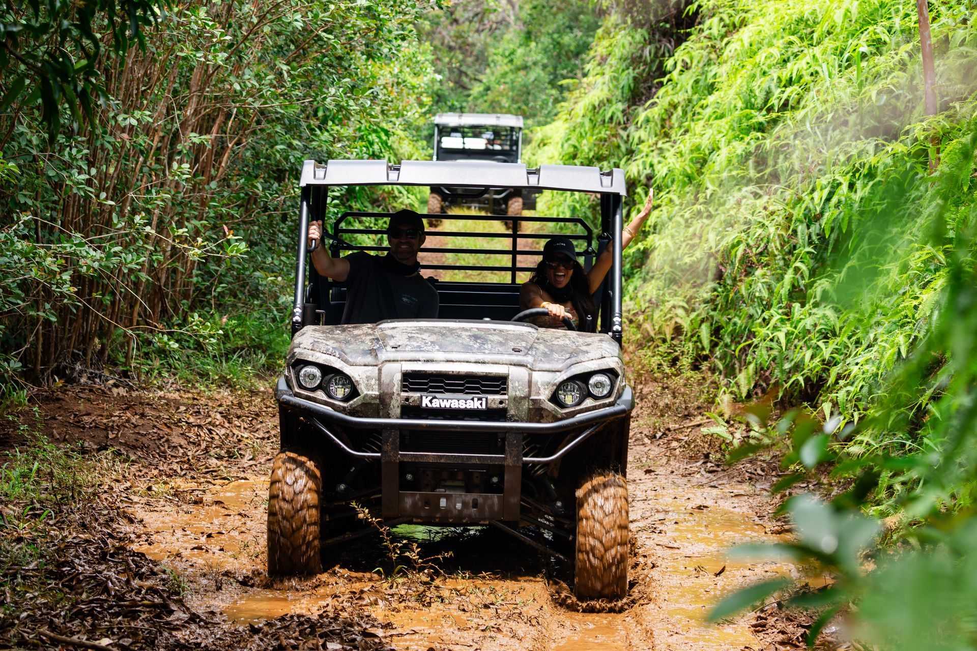 Off-road vehicle driving through a muddy forest trail with two passengers