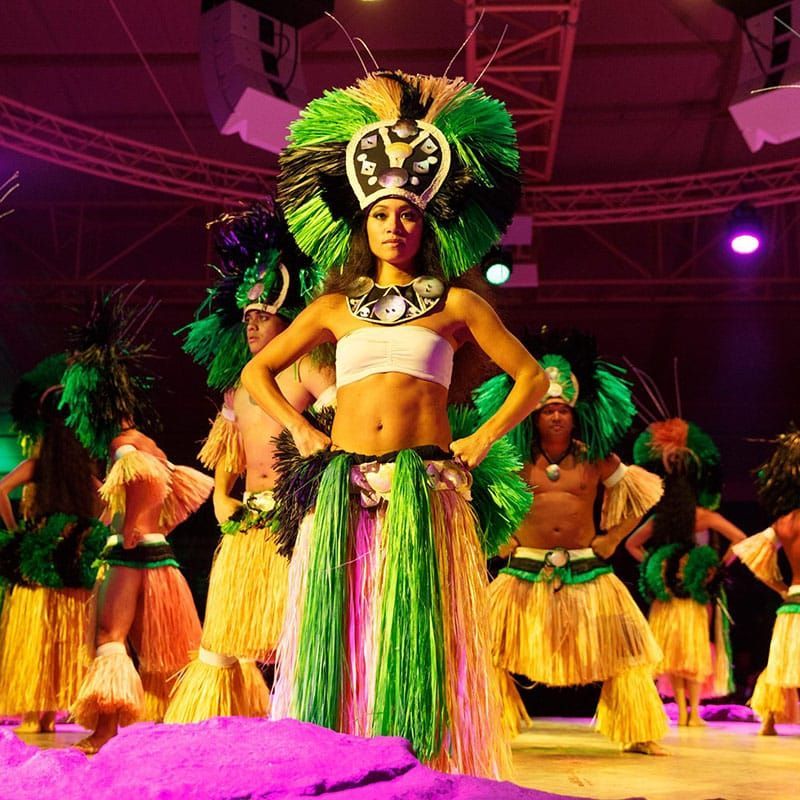 Costumed dancers performing on stage in green, yellow, and purple carnival outfits