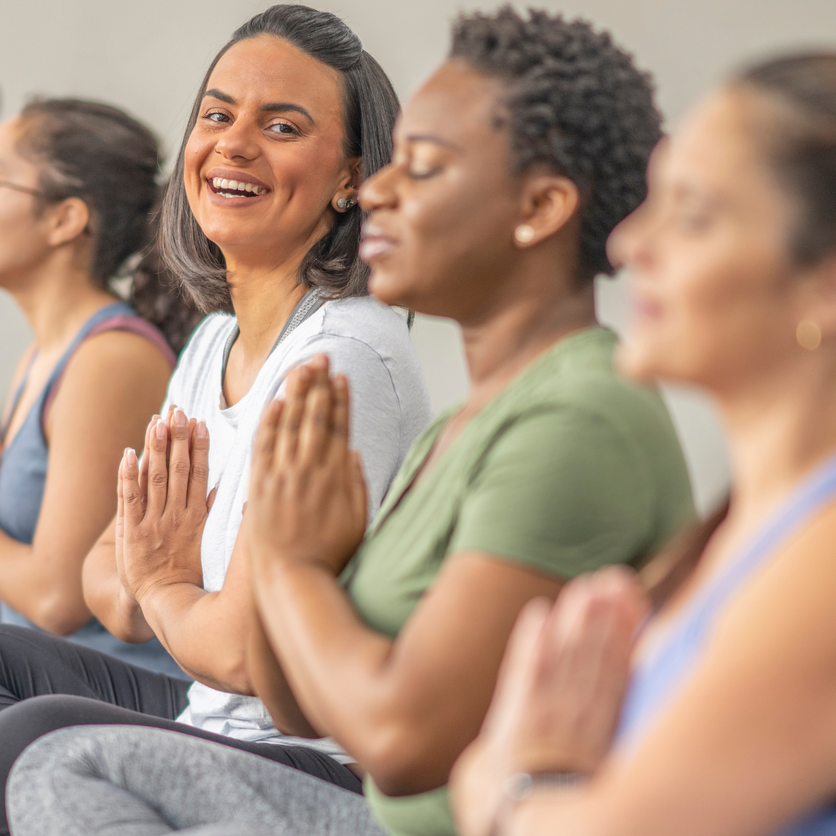A group of women are sitting in a row with their hands folded in prayer.
