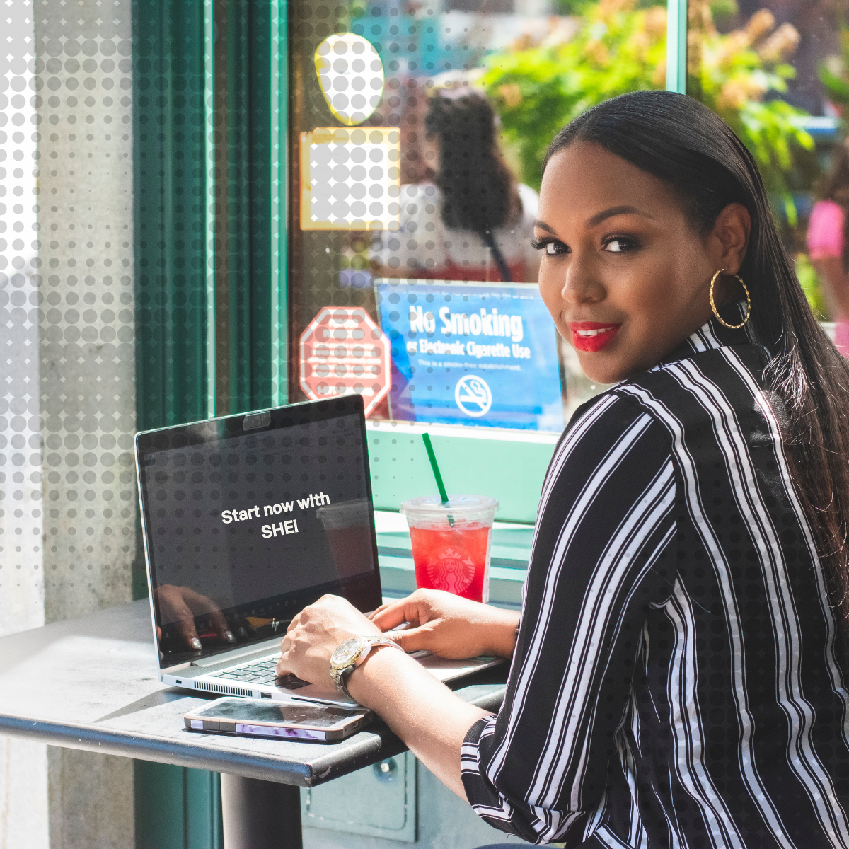 A woman is sitting at a table with a laptop and a drink.