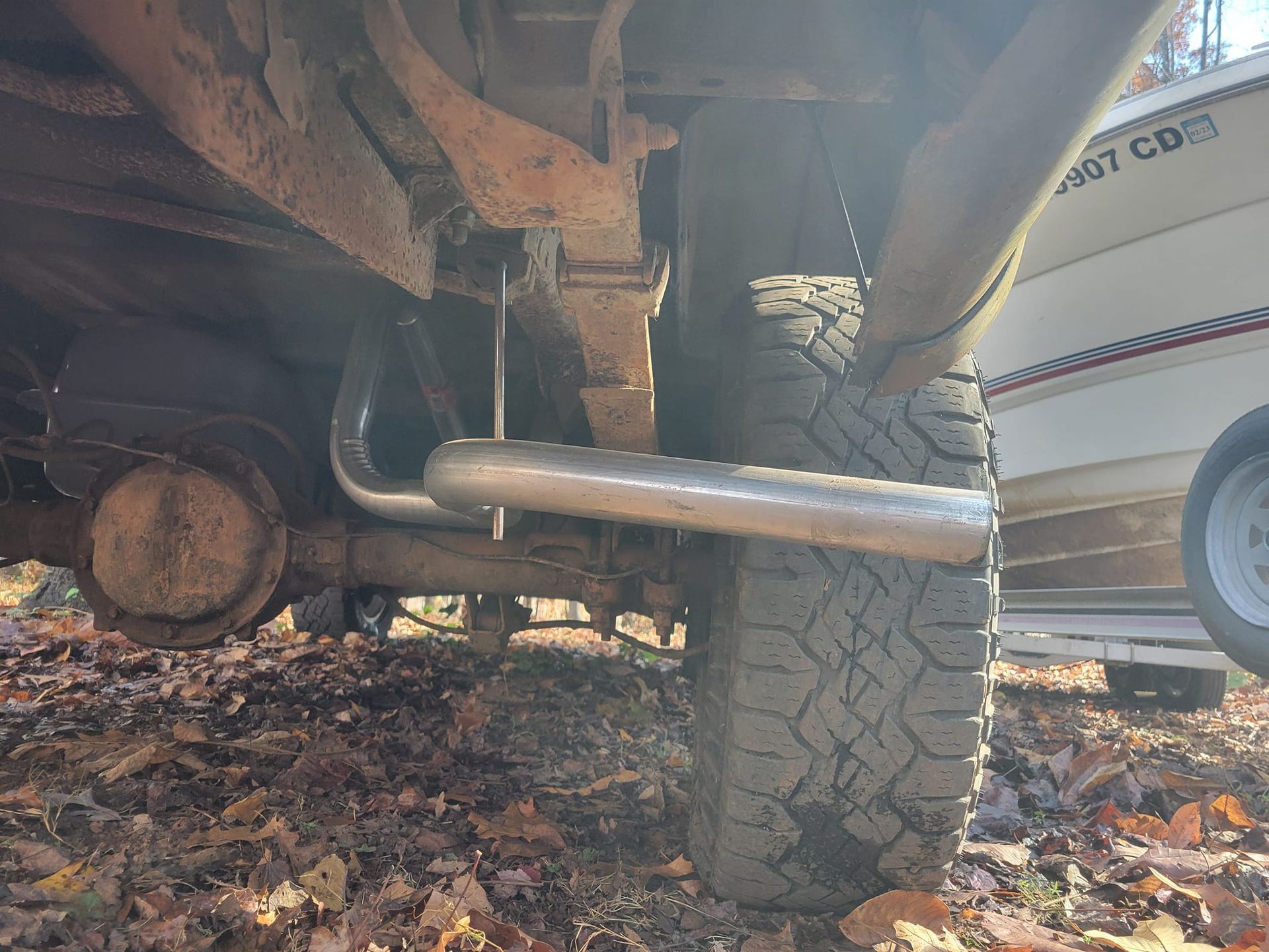 A close up of the underside of a truck with a boat in the background.