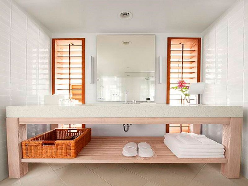 Bathroom vanity with light wood frame, white counter, basket, towels, and shutters.