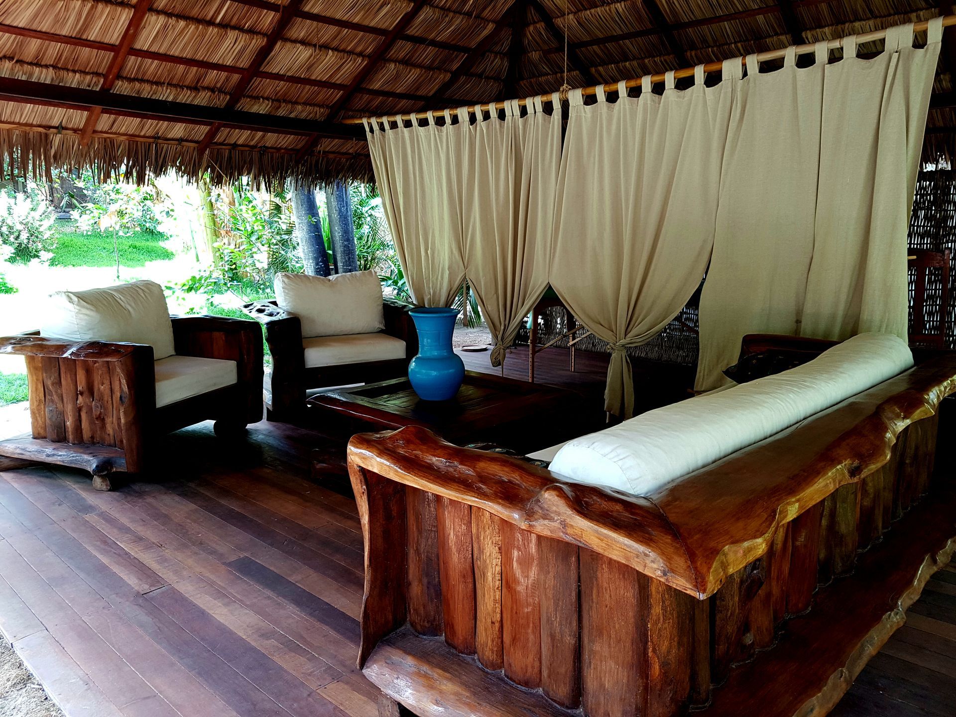 Outdoor seating area with wood furniture and thatched roof.