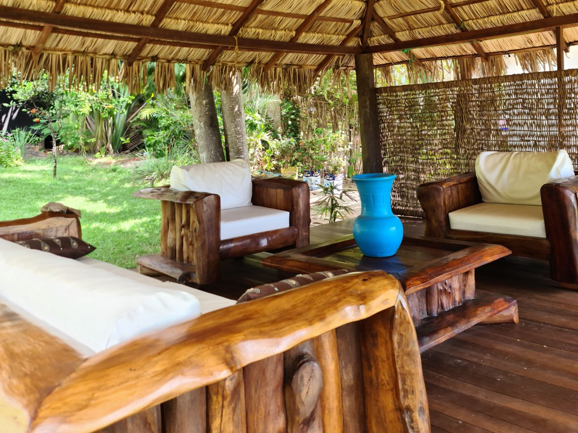 Wooden outdoor seating under a thatched roof gazebo, with blue vase on the coffee table.