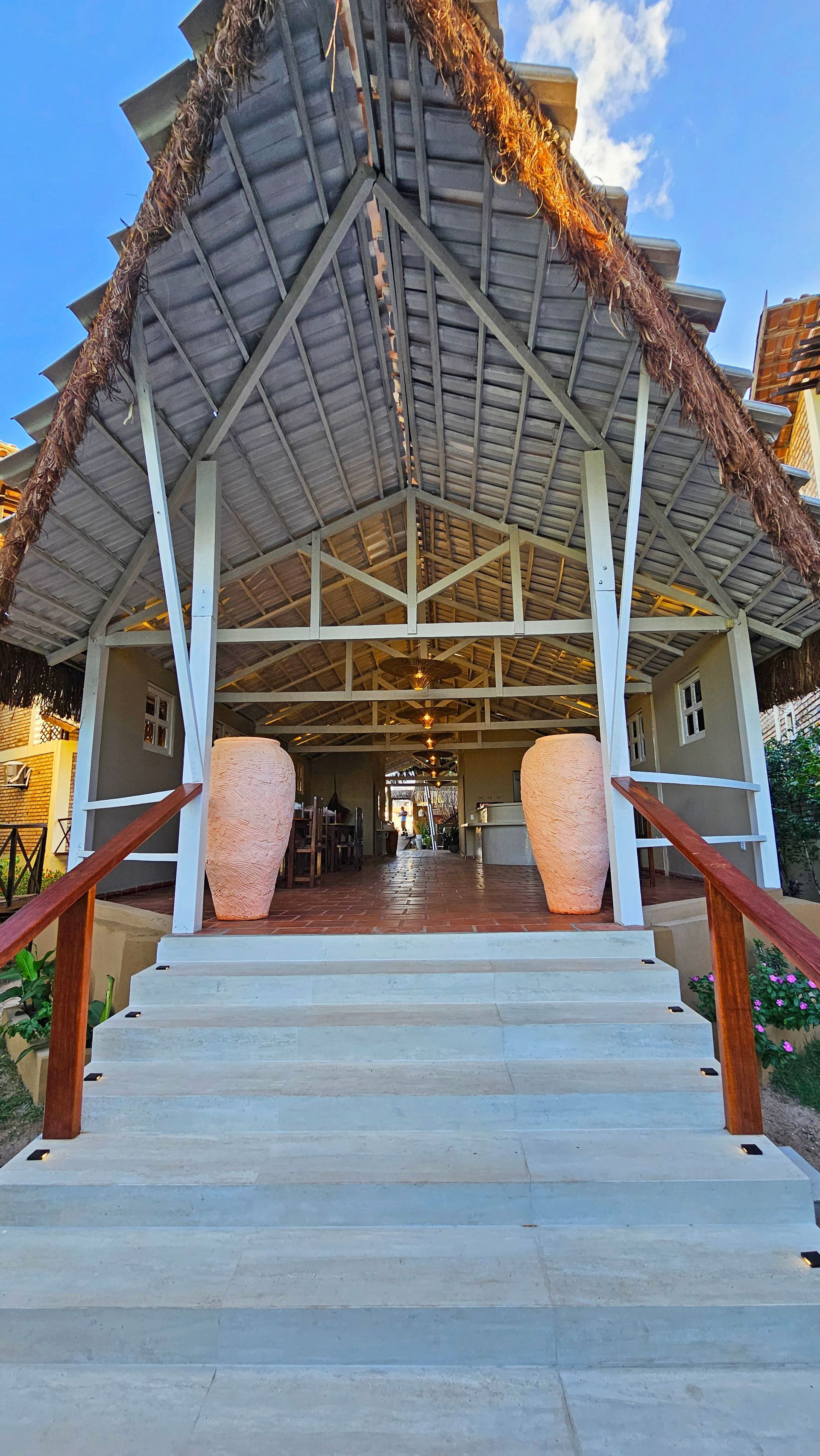 Entrance with steps, thatch roof, large vases, and a view into a restaurant with tables.