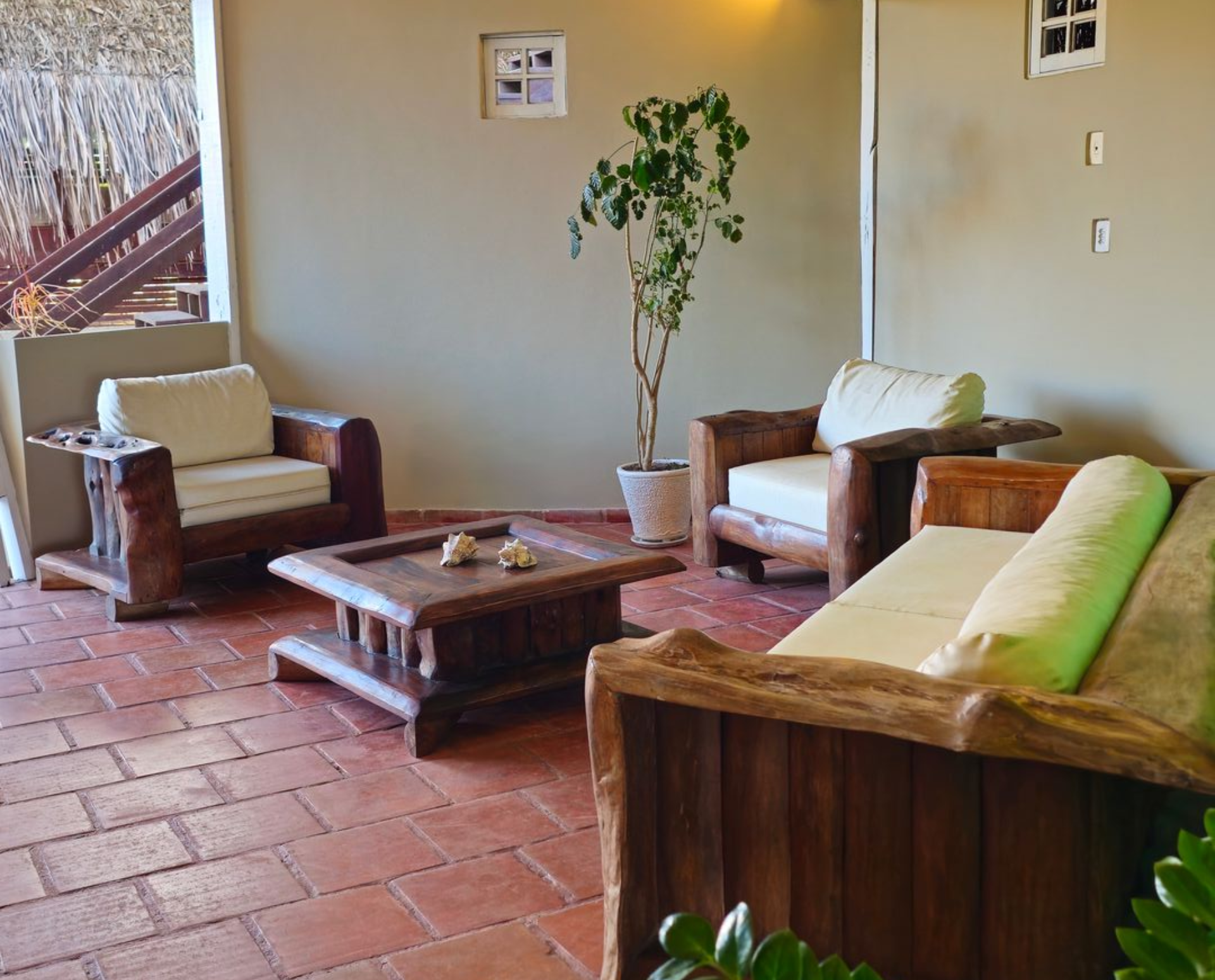 Outdoor seating area with wooden furniture, terracotta tile floor, and potted plant.