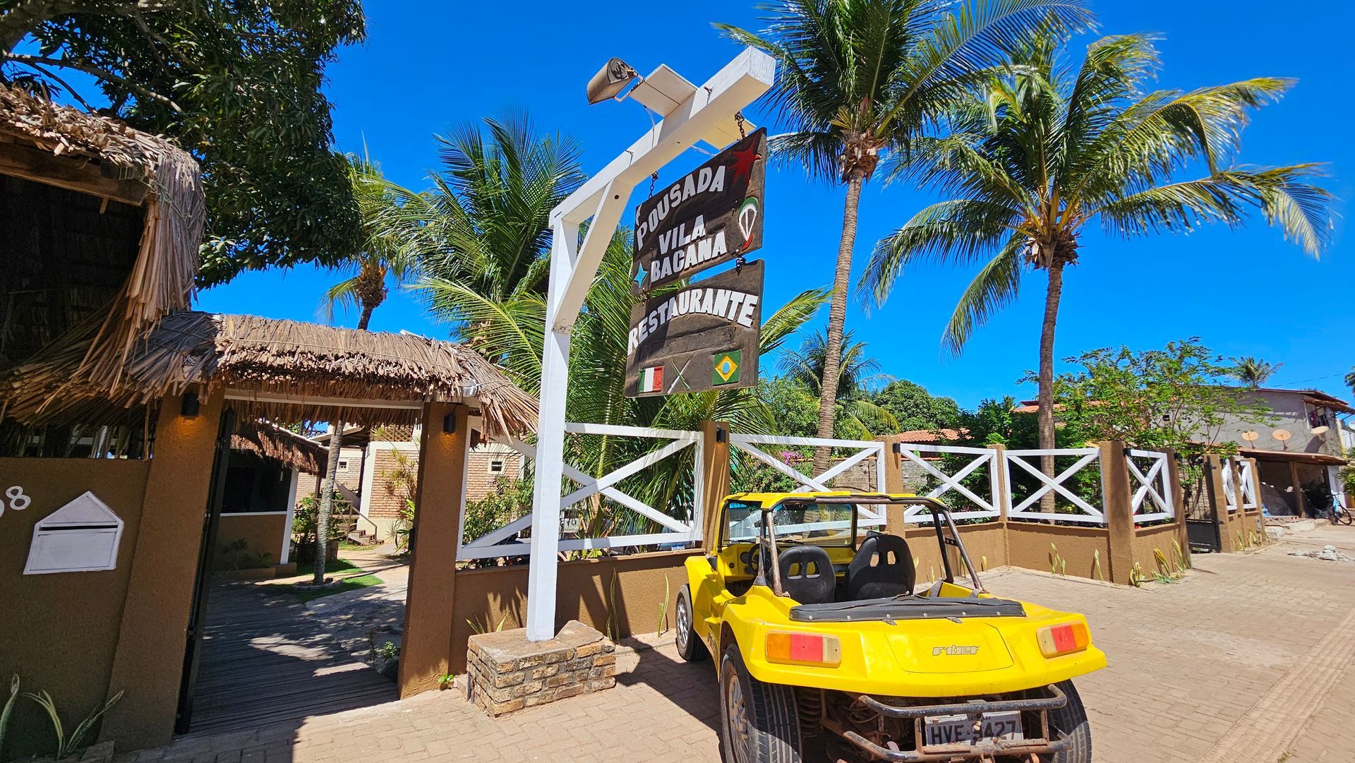Yellow buggy parked near a sign with writing, tropical setting with palm trees.
