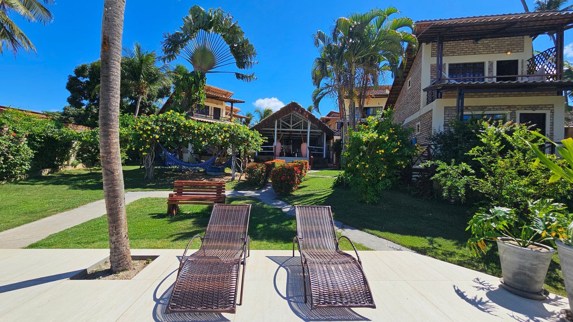 Two lounge chairs face a grassy lawn and buildings with a clear blue sky.