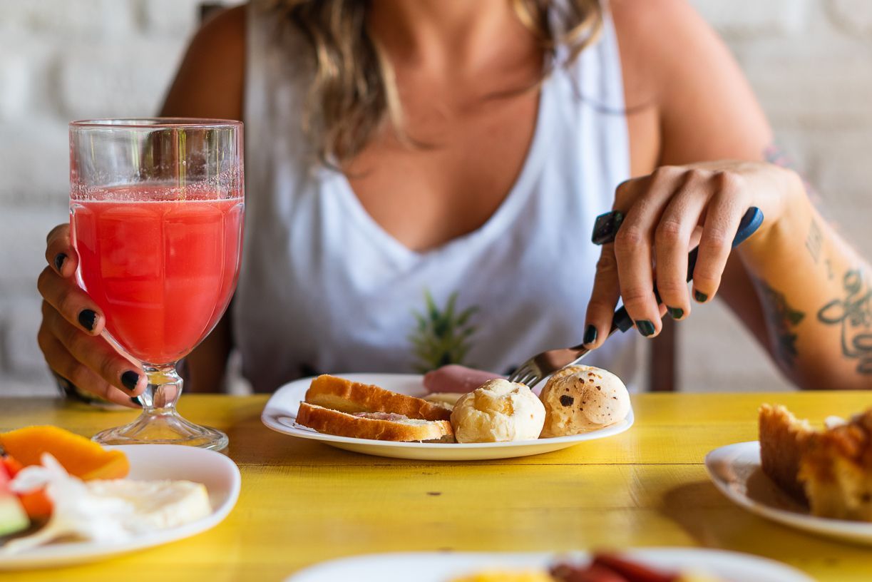 Woman eating breakfast, cutting food on a plate at a yellow table; a glass of juice and other dishes visible.