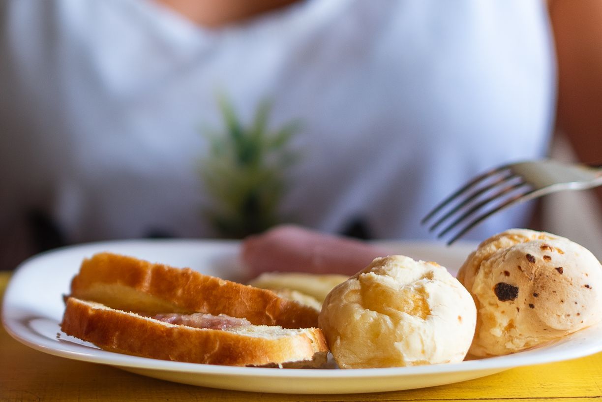 Plate with toasted bread, cheese puffs, and ham; person holding fork.