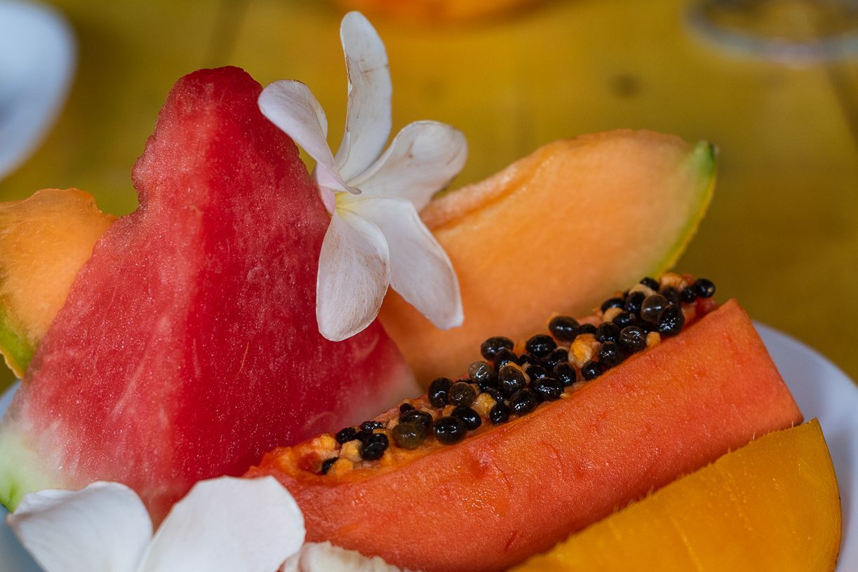 Sliced fruit, including watermelon, cantaloupe, and papaya, is garnished with a white flower.