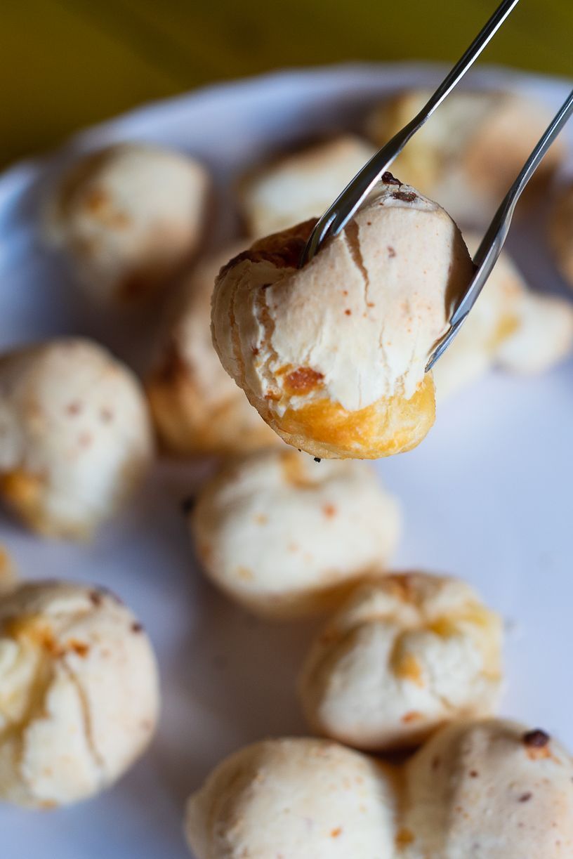 Cheese bread rolls being held by tongs. White plate, yellow background.