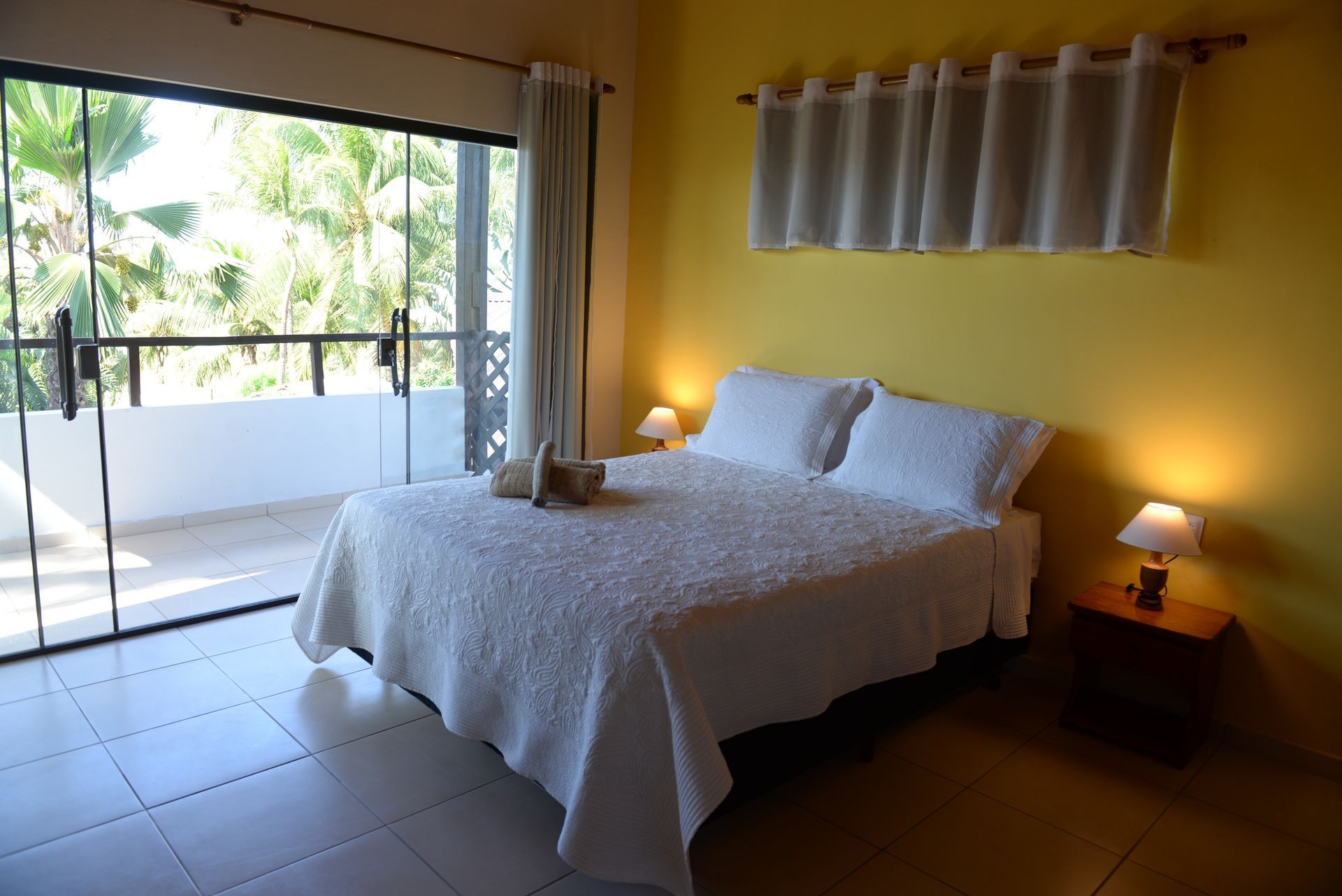 Bedroom with yellow walls, white bedspread, balcony access, and two bedside lamps.