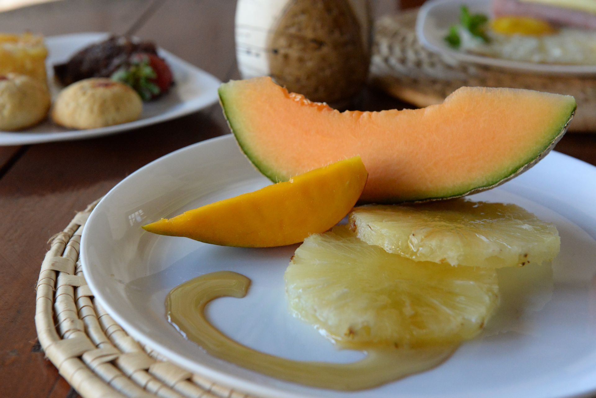 Plate of fruit: melon, mango, pineapple, drizzled with syrup.