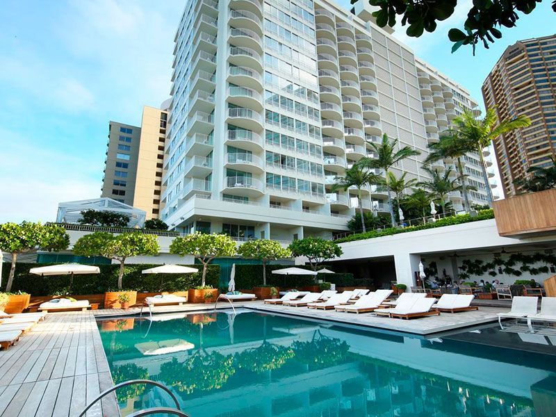 Swimming pool and lounge chairs at a luxury hotel, with a multi-story building in the background.