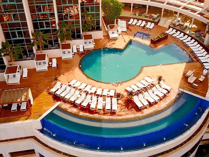 Aerial view of a hotel pool deck with a tiered pool, lounge chairs, and buildings.