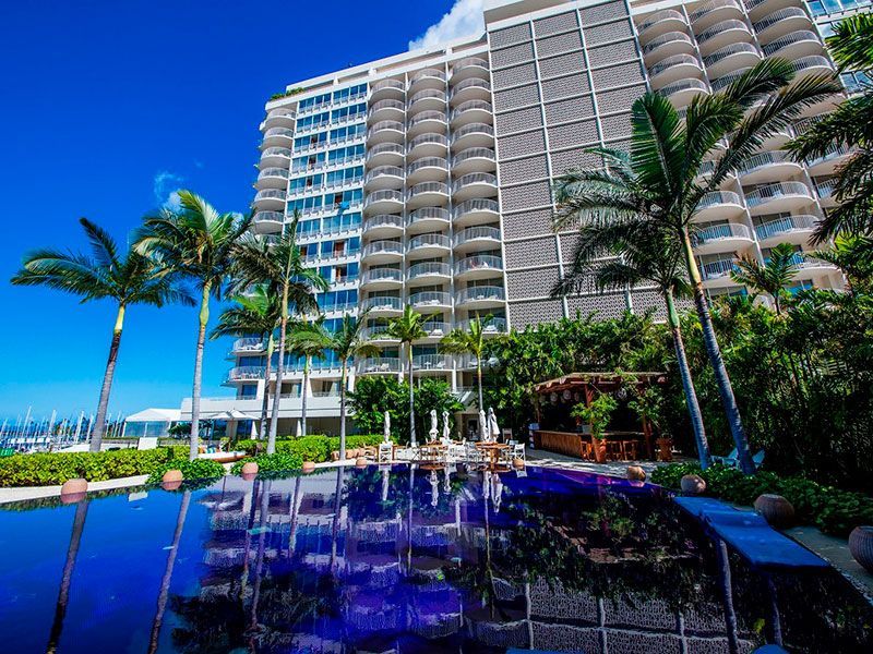 Hotel exterior with pool, palm trees, and blue sky reflection.