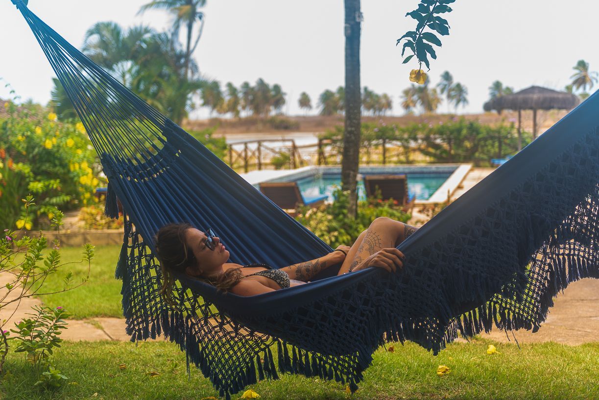 Woman relaxing in a blue hammock on a sunny day near a pool and greenery.