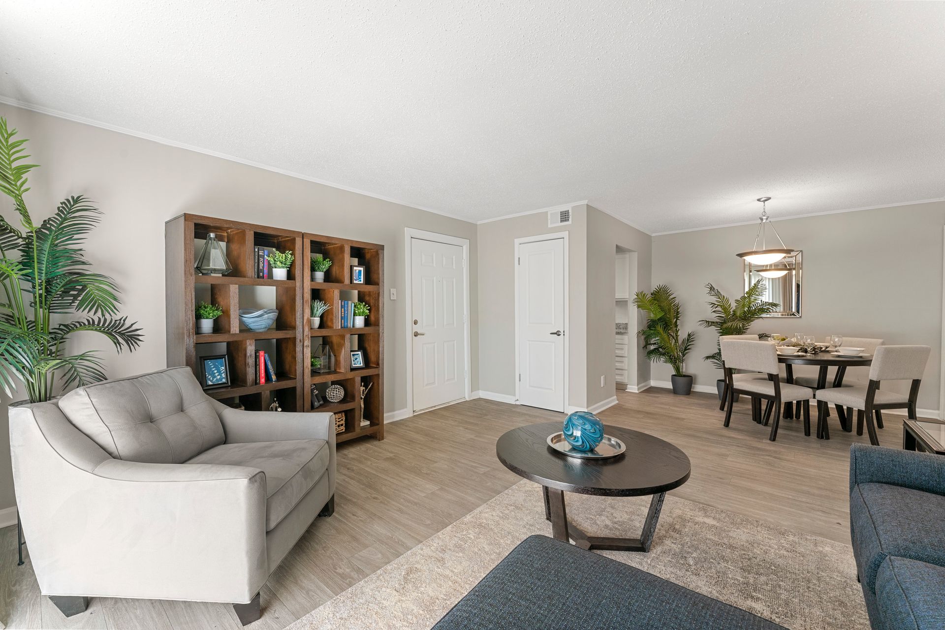 Bright living room with beige sofa, bookshelves, coffee table, and dining area in the background