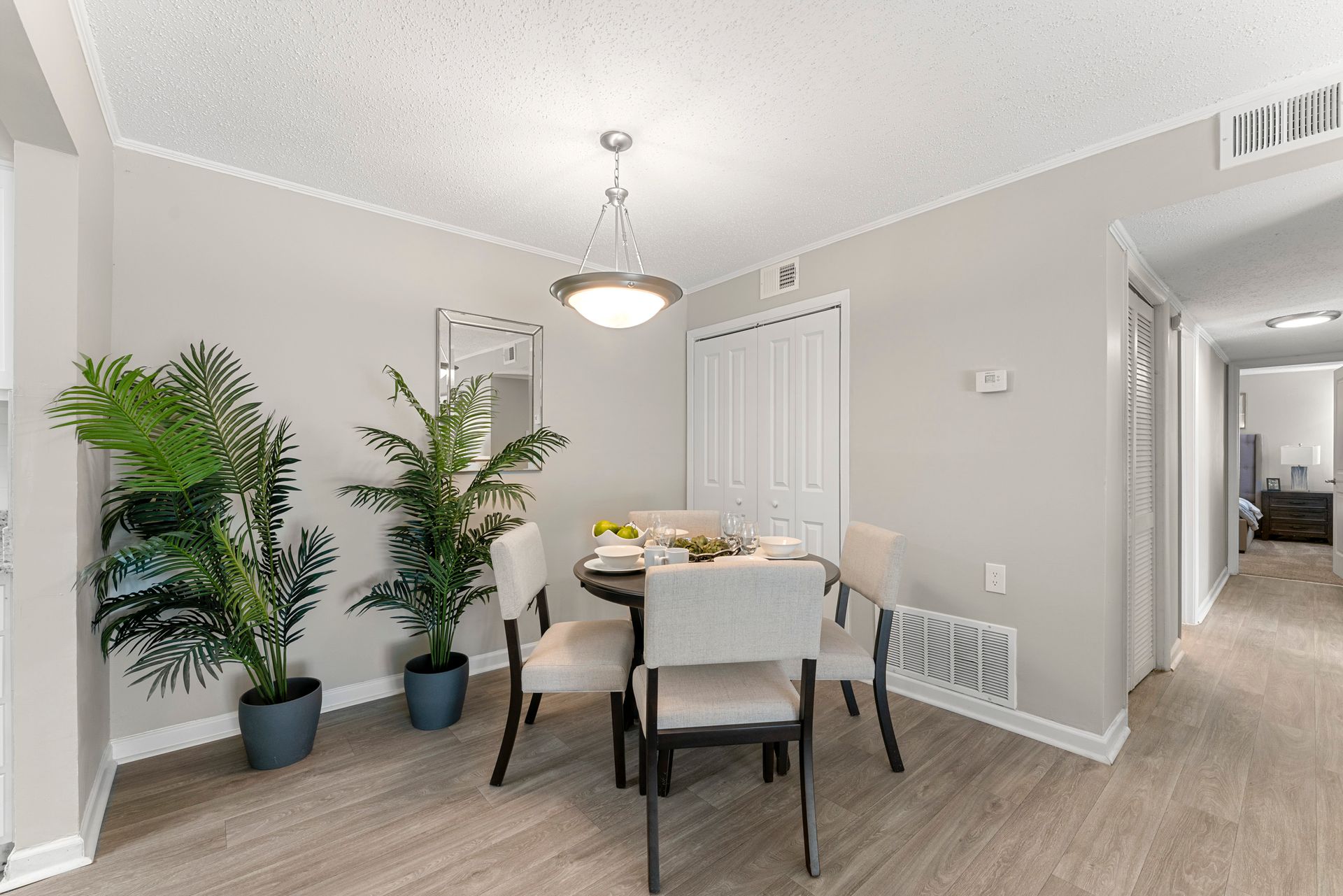 Modern dining room with round table, beige chairs, potted plants, and light gray walls.