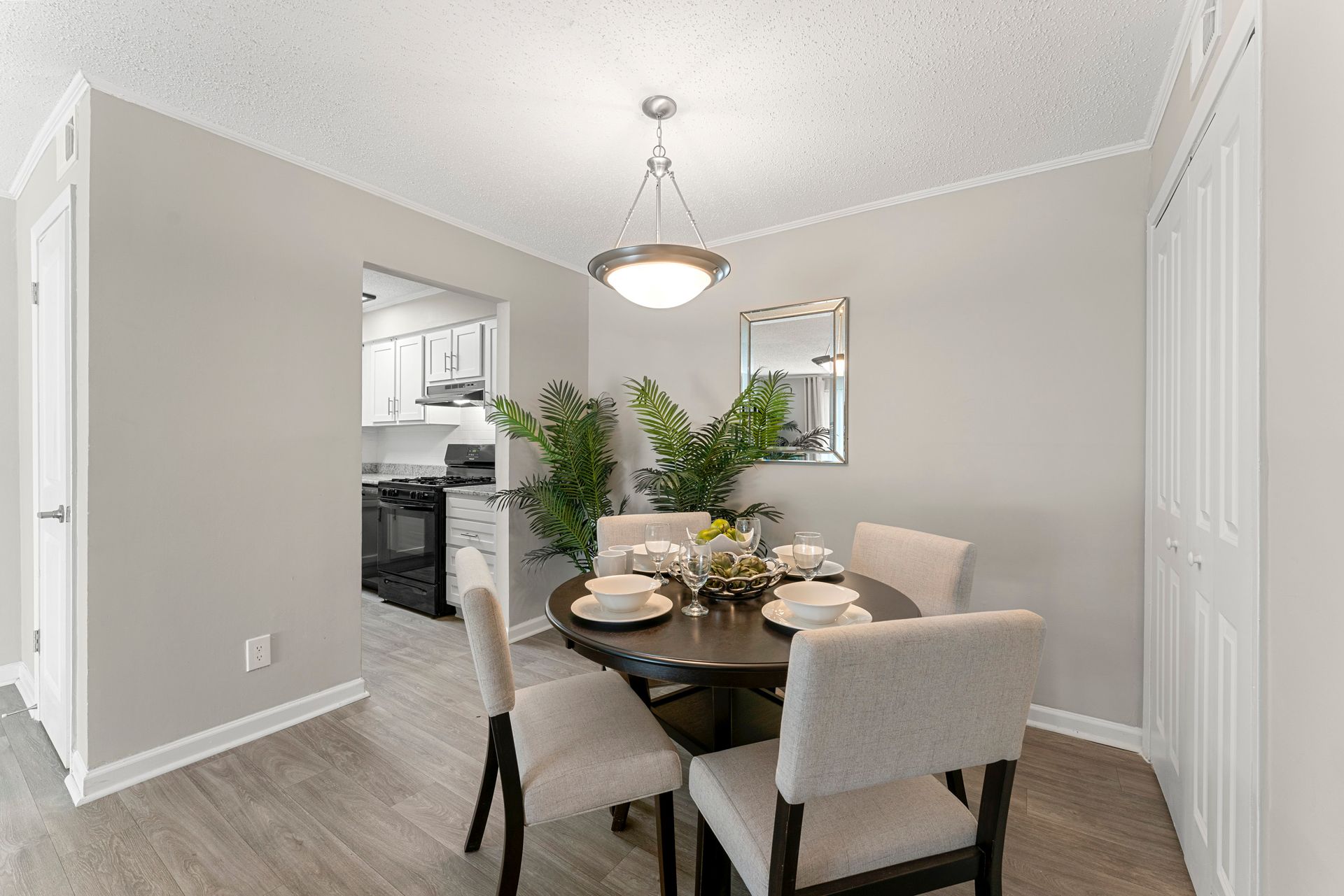 Dining room with dark table, beige chairs, chandelier, and potted plant in a bright neutral home.