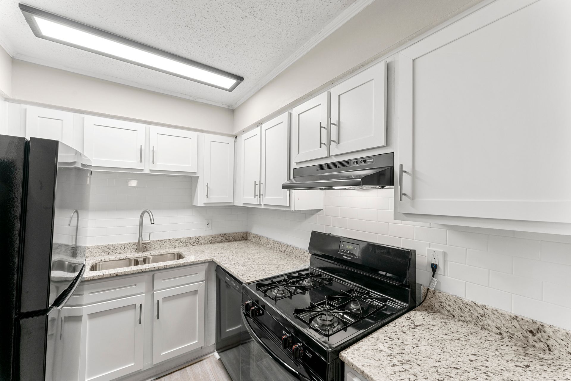 Bright white kitchen with granite countertops, black stove, and white cabinets under a ceiling light.