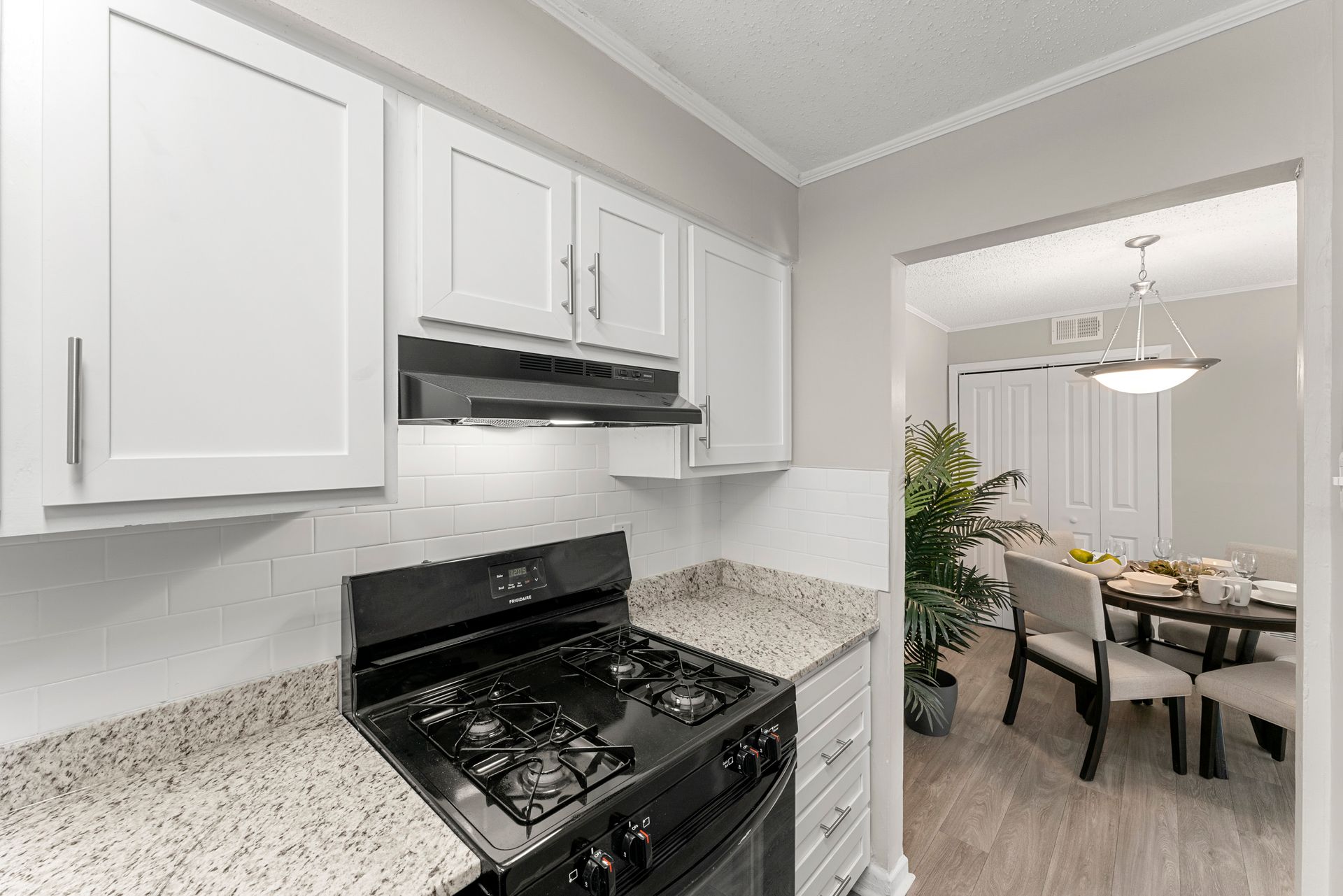 Bright kitchen with white cabinets, black stove, and a view into a dining room beyond.
