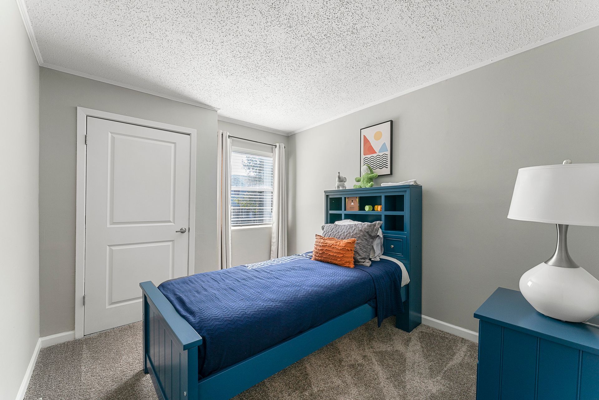 Small blue bedroom with a twin bed, white door, and blue shelving against gray walls.
