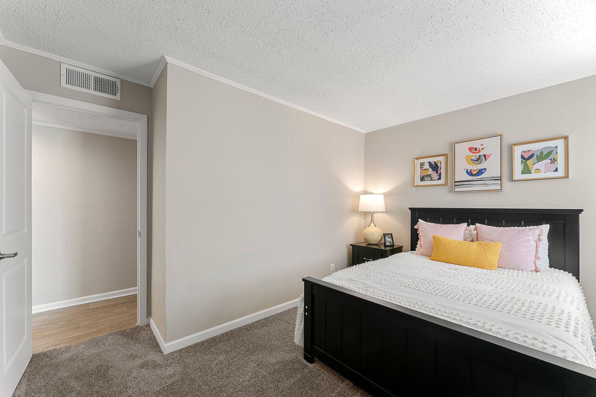 Bedroom with a black bed, yellow pillow, bedside lamp, and three framed pictures on a light wall.